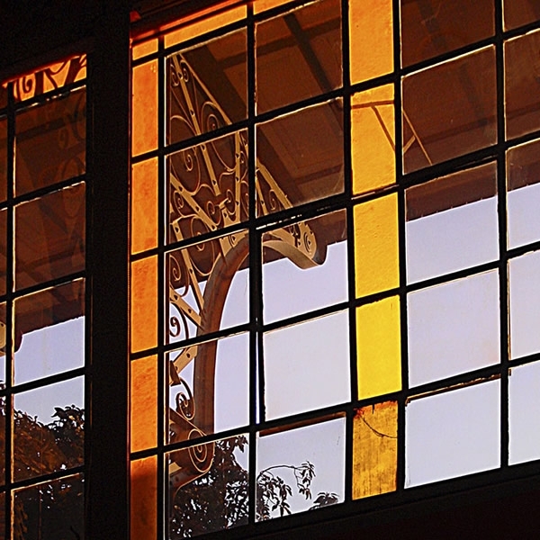 Grid of colored glass panels reflecting a metal ornament and trees at dusk