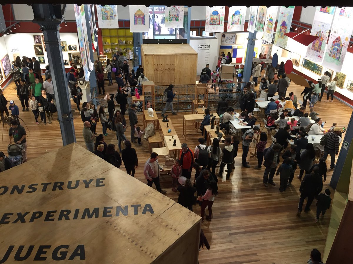 Overhead view of the crowded exhibition hall with wooden displays and visitors gathered around workshop tables