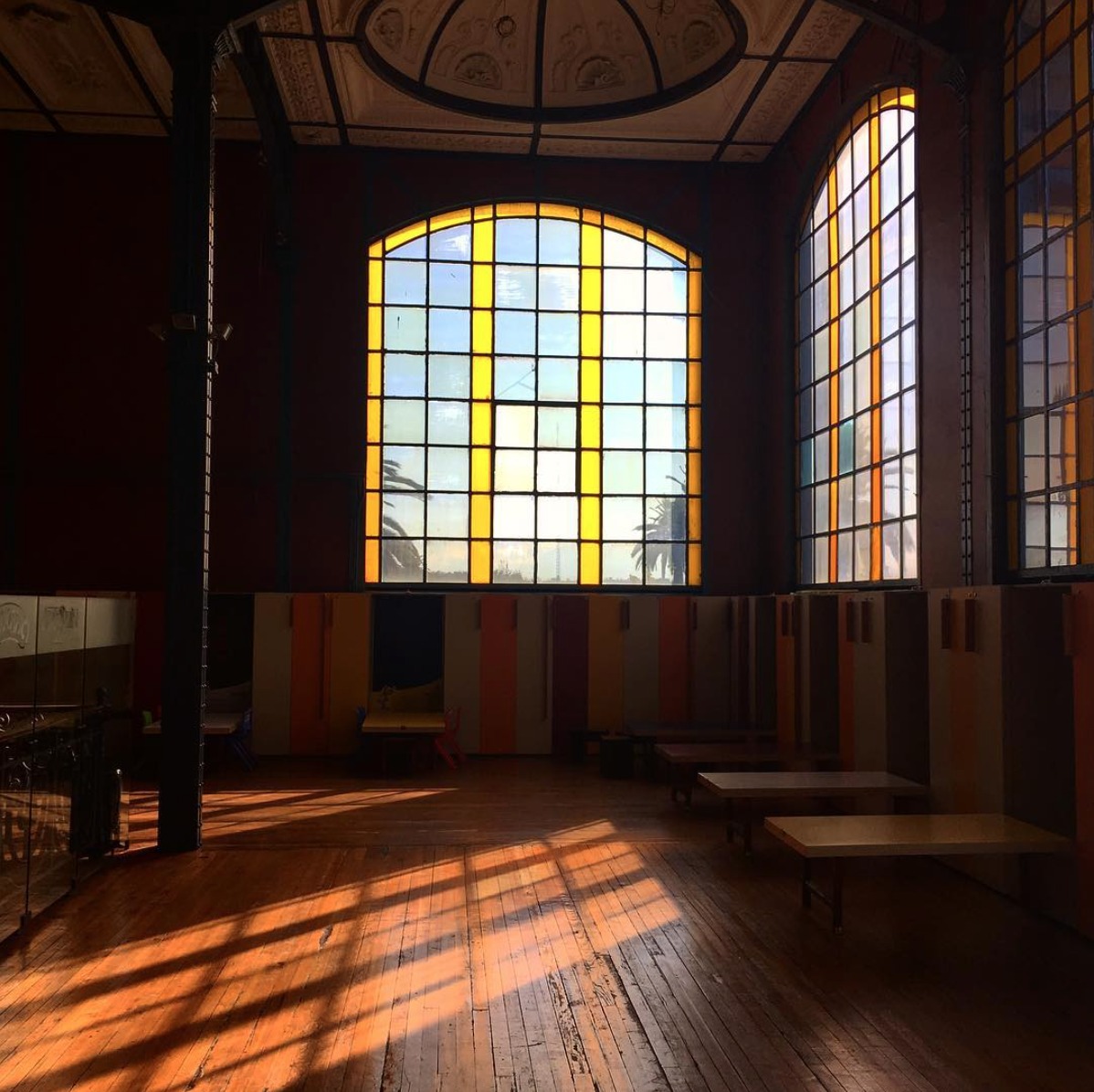 Gallery room with tall arched gridded windows casting geometric shadows across the timber floor