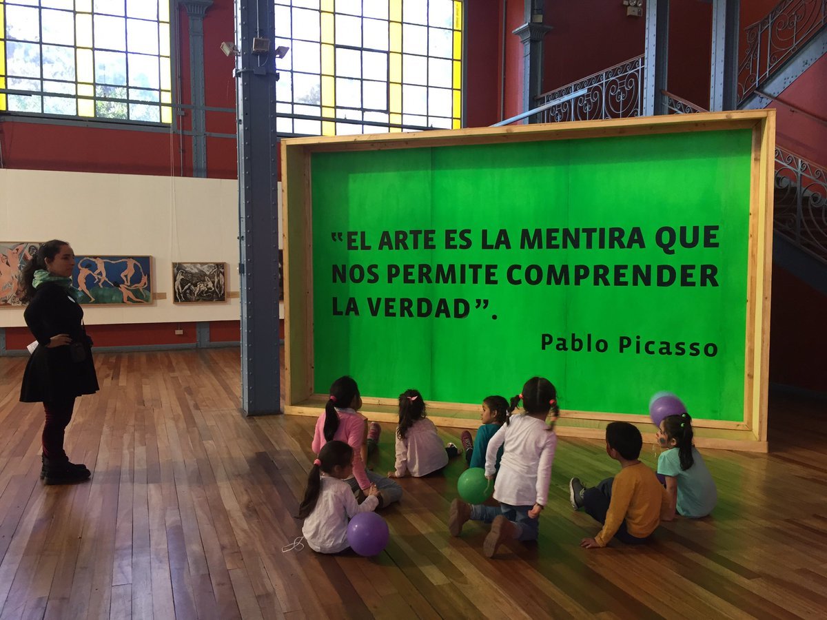 Children seated on the floor before a green display panel with quotation text beneath the steel columns