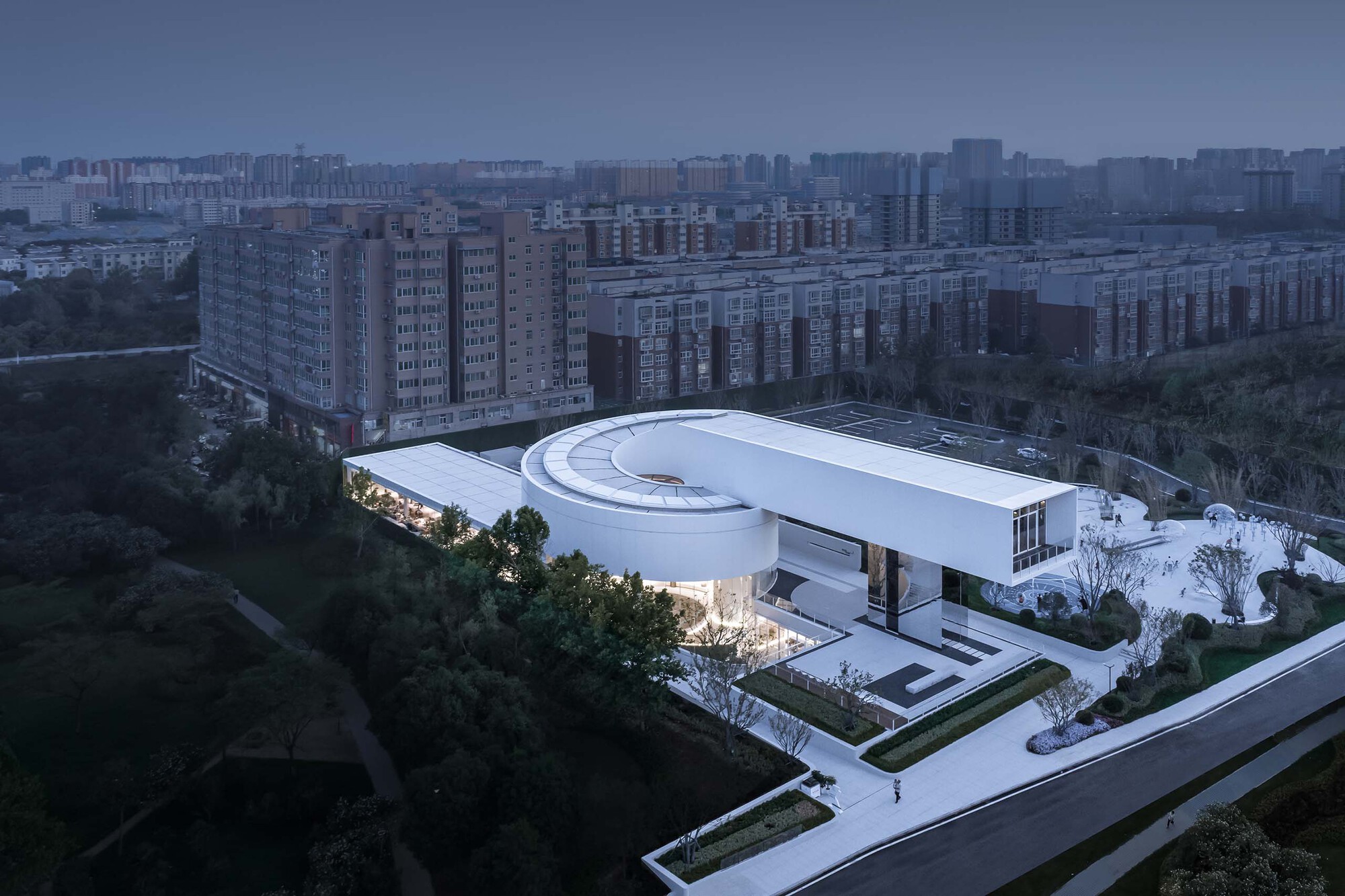 Aerial view of the curved roof with circular skylight and green courtyards at dusk