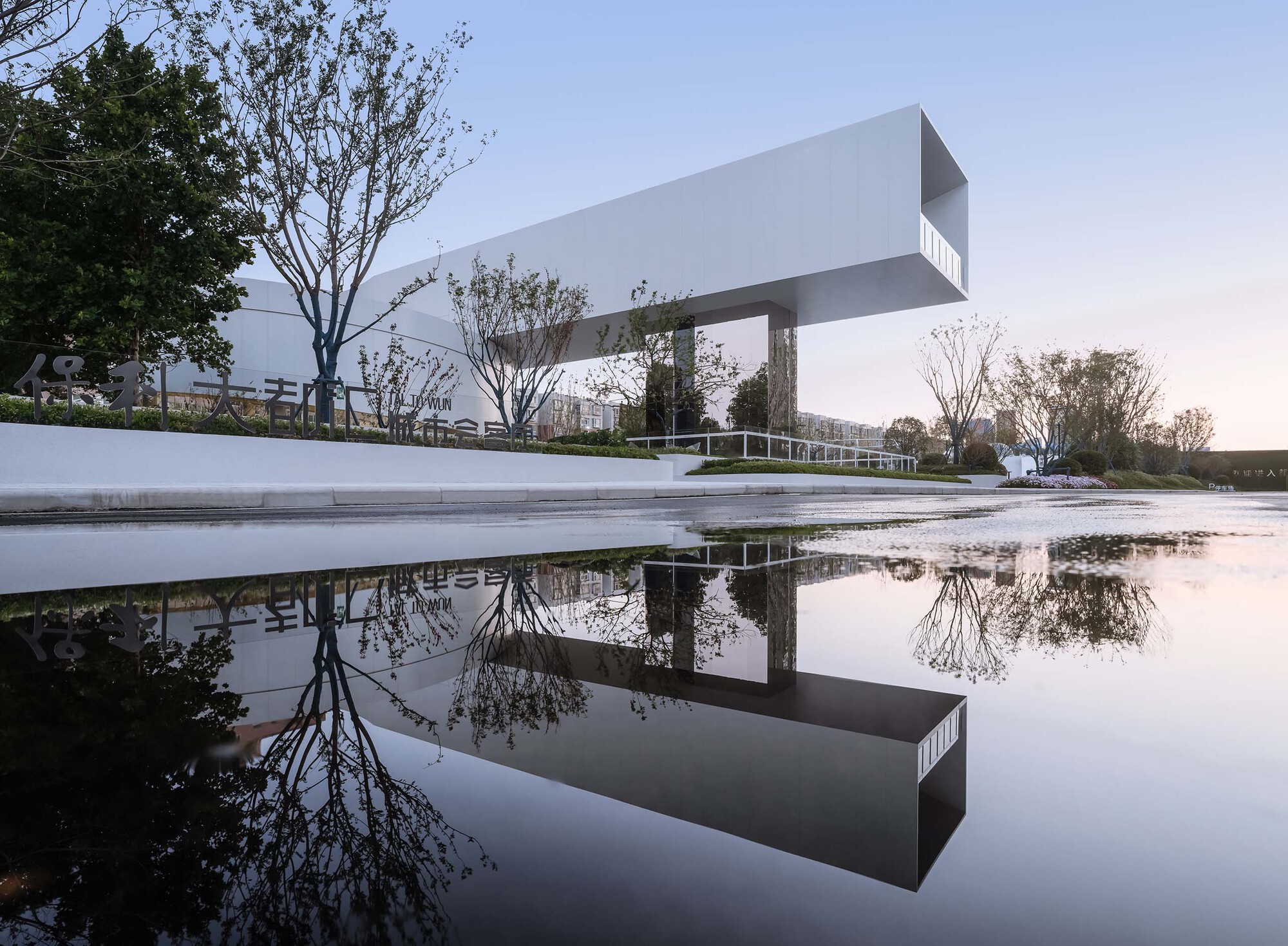Cantilevered white volume on columns reflected in still water at dusk with bare trees