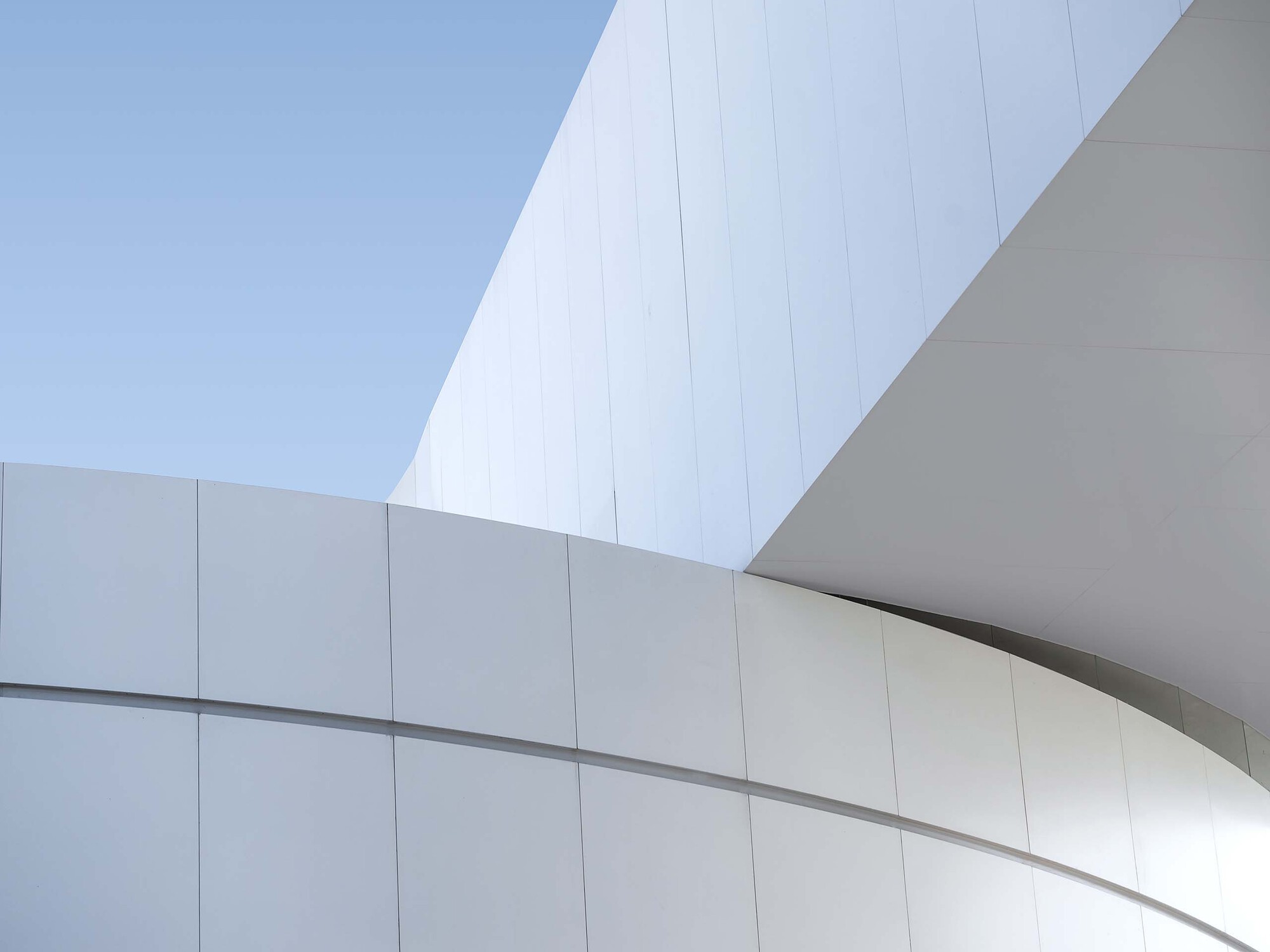 White paneled facade with curving forms meeting at angular junction in bright daylight