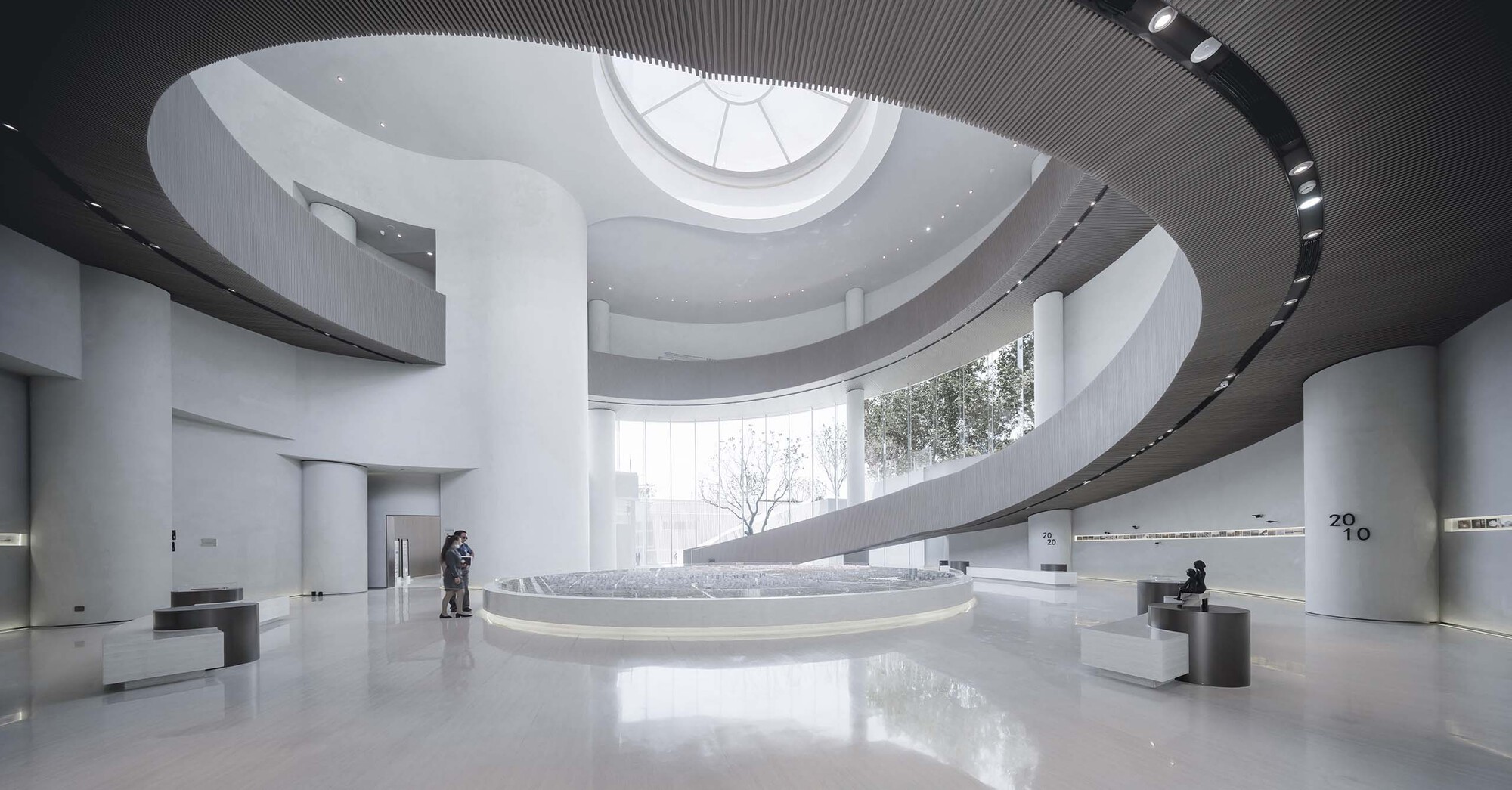 Double-height atrium with spiraling ramp around a circular skylight and visitors below