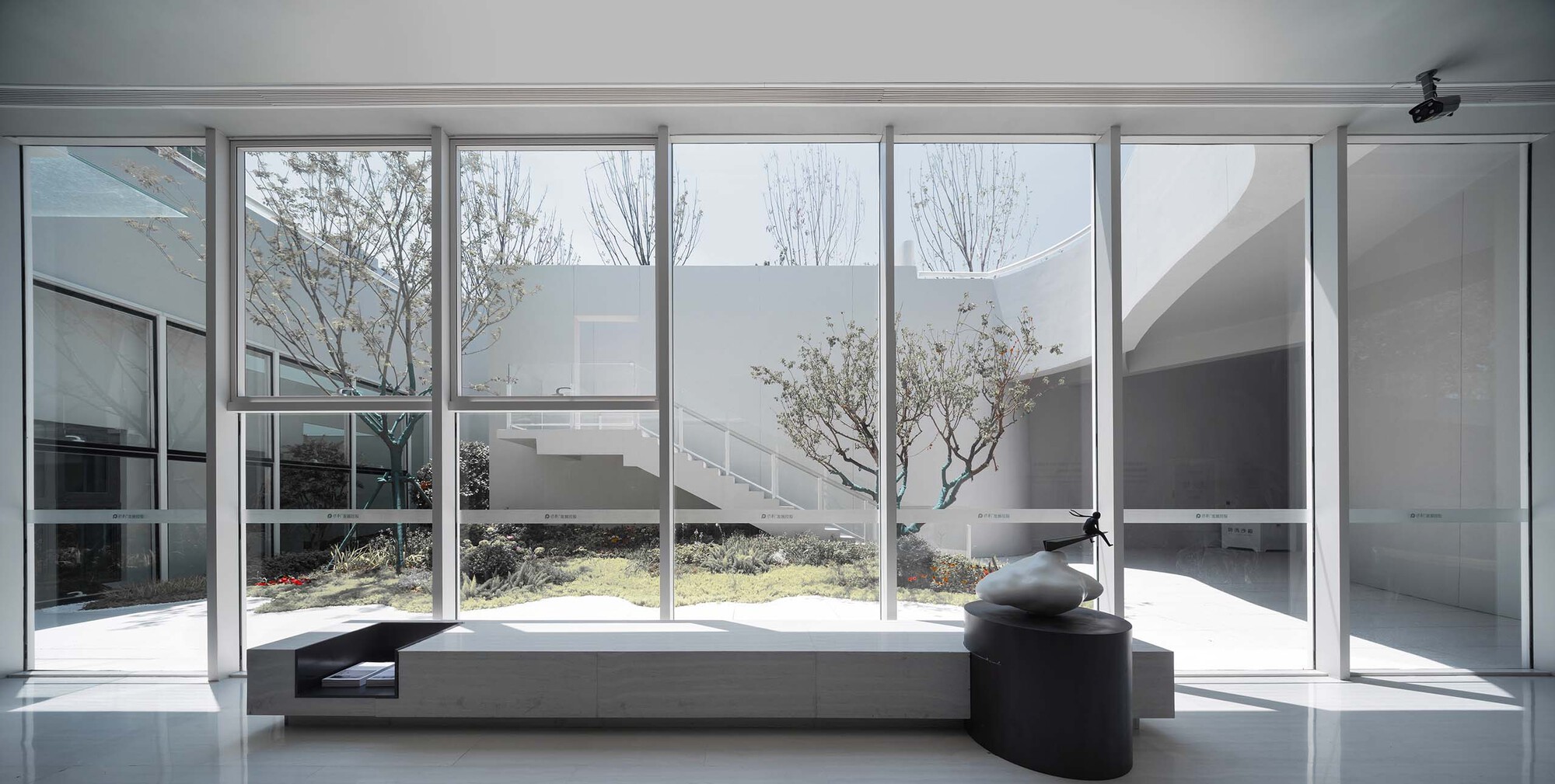 Floor-to-ceiling glass wall framing an interior courtyard with bare trees and stone benches
