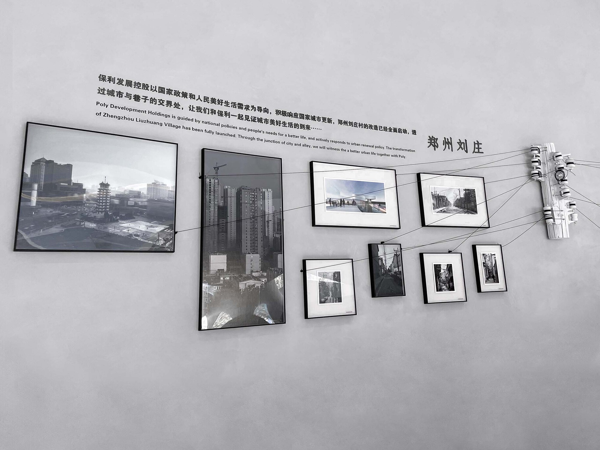 Gallery wall with framed photographs suspended on cables beneath a utility pole fragment