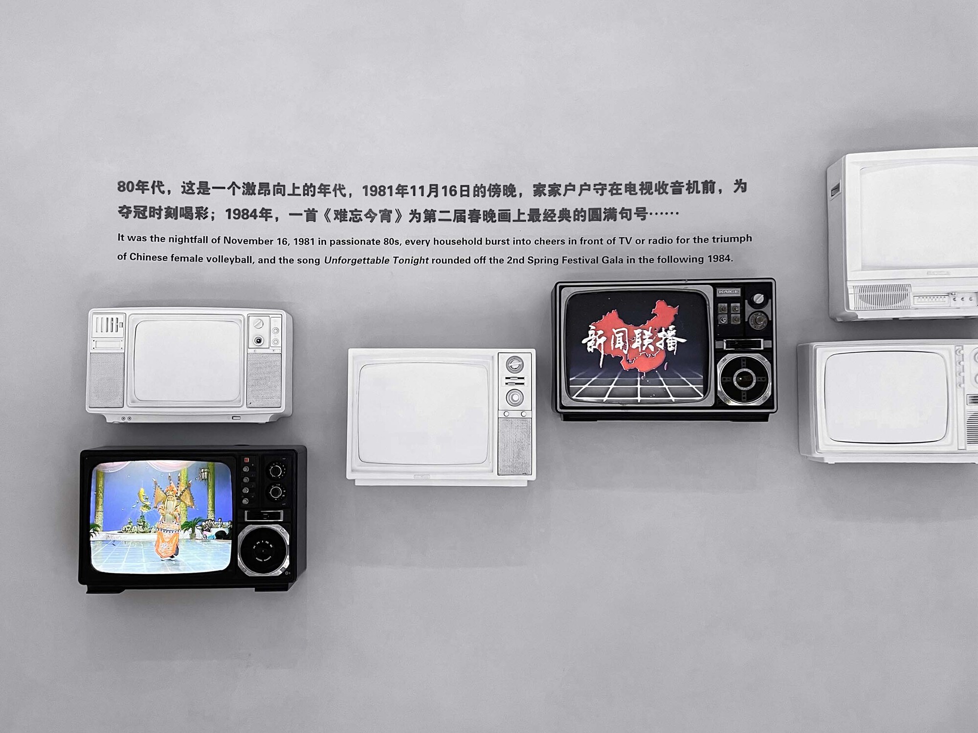 Wall display of vintage television sets mounted on a grey surface with Chinese text above