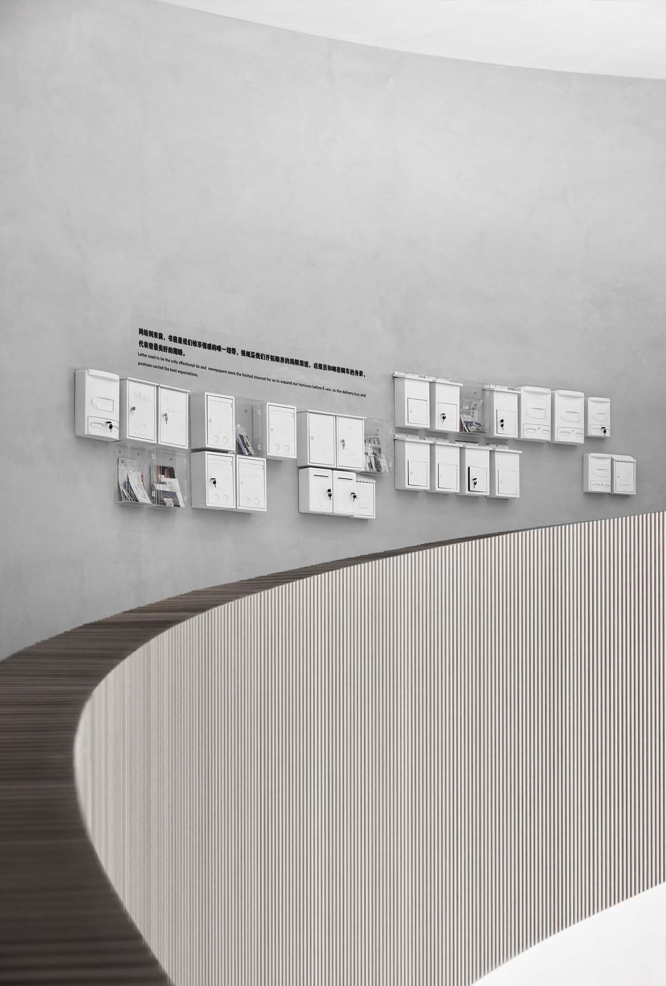 Curved reception desk with vertical wood slat cladding beneath a grid of white-framed display panels