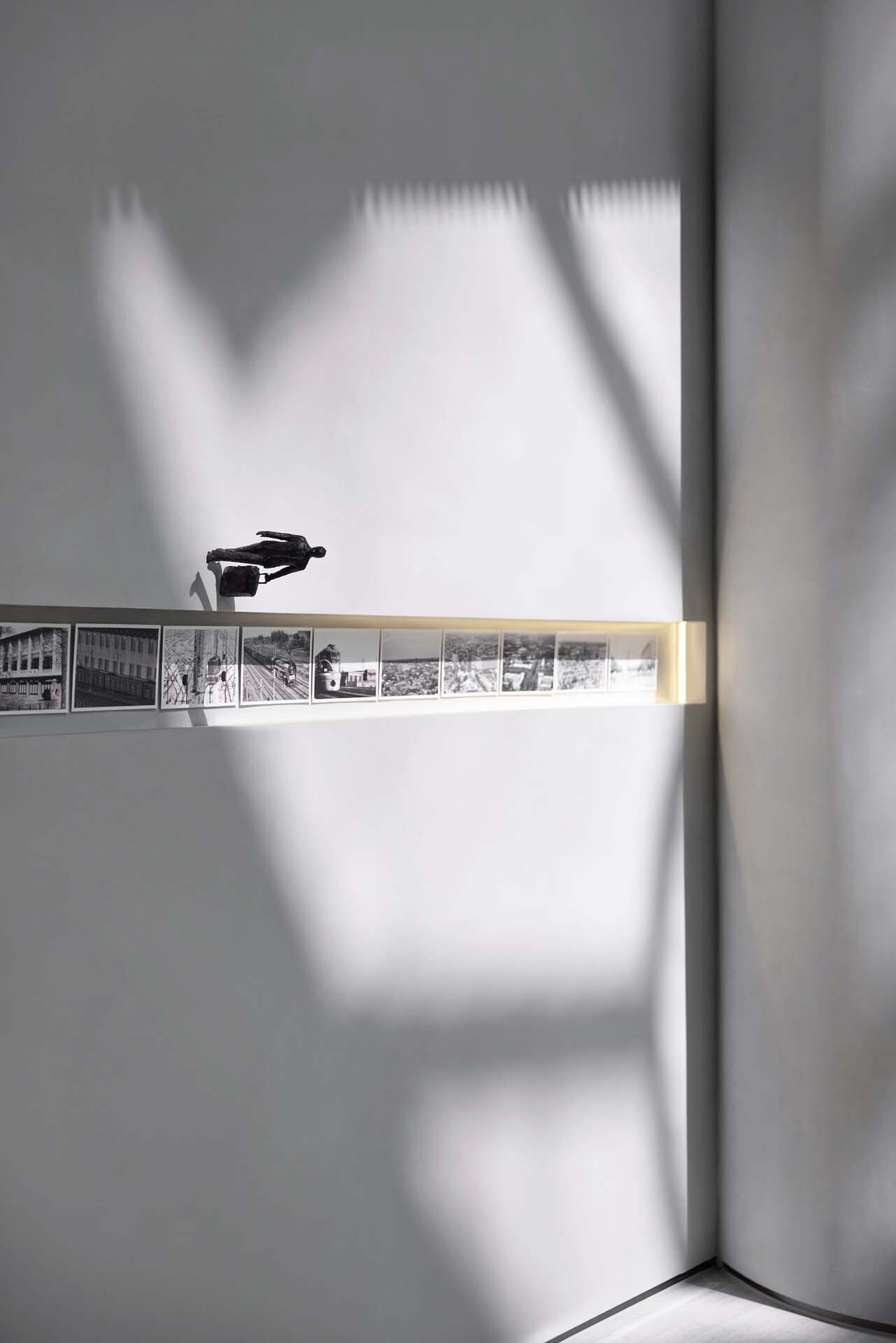 Corner detail of illuminated horizontal display strip with archival photographs casting shadows on white walls