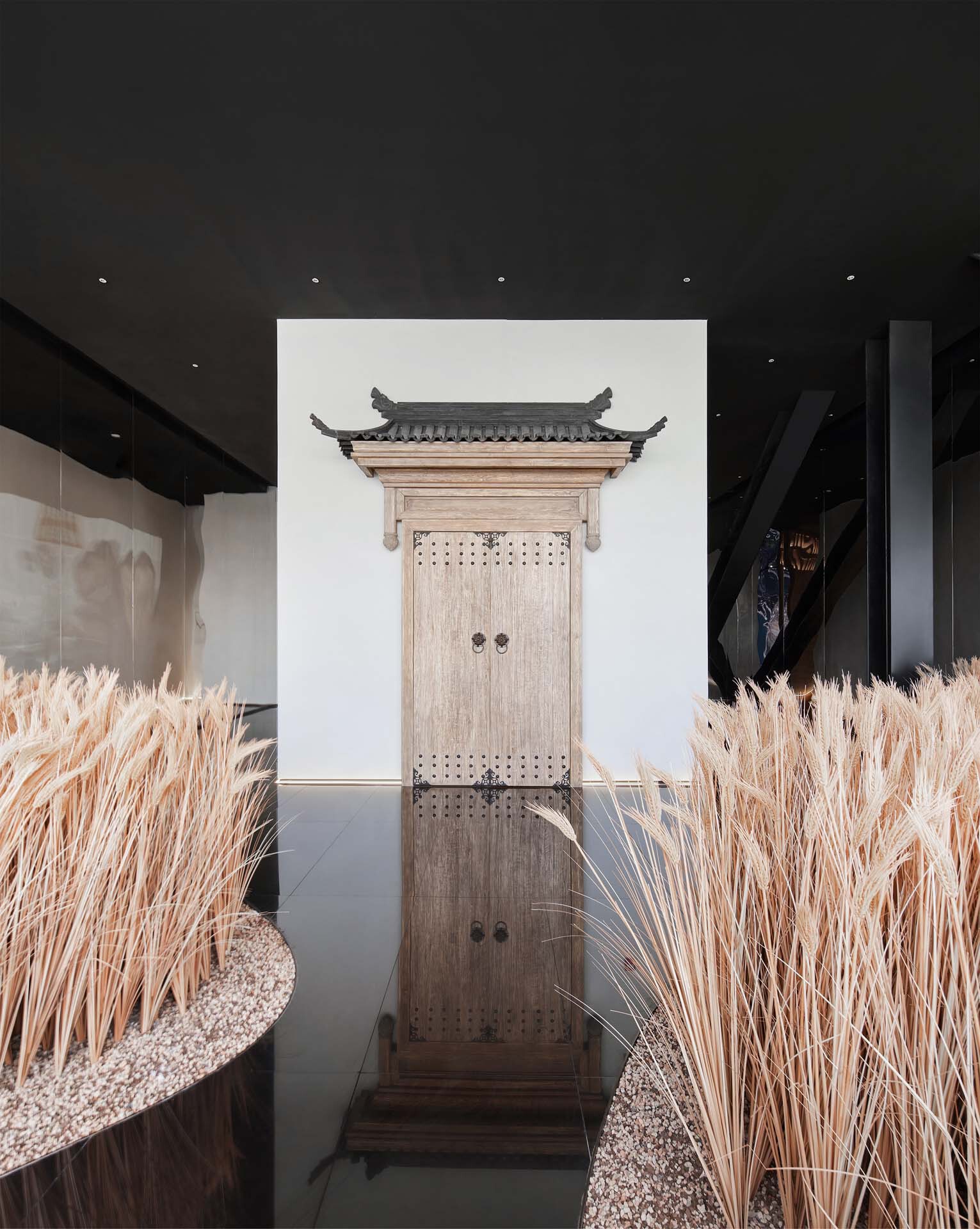 Exhibition hall with traditional timber door beneath curved roof against a white backdrop and dried grasses