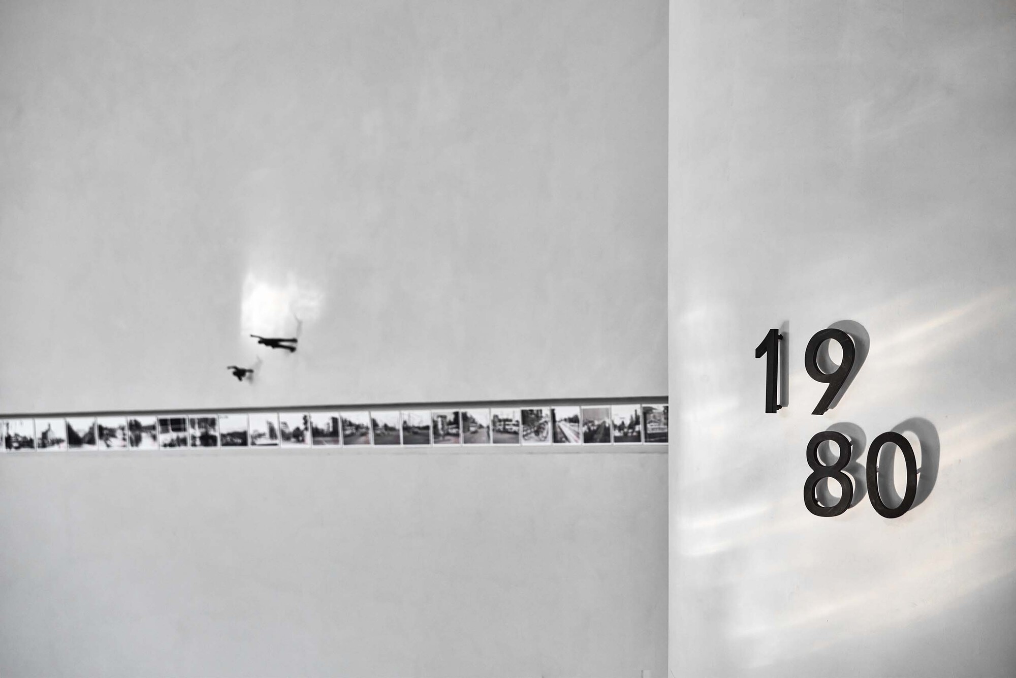 Wall detail showing backlit numerals reading 1980 beside a horizontal strip of archival photographs