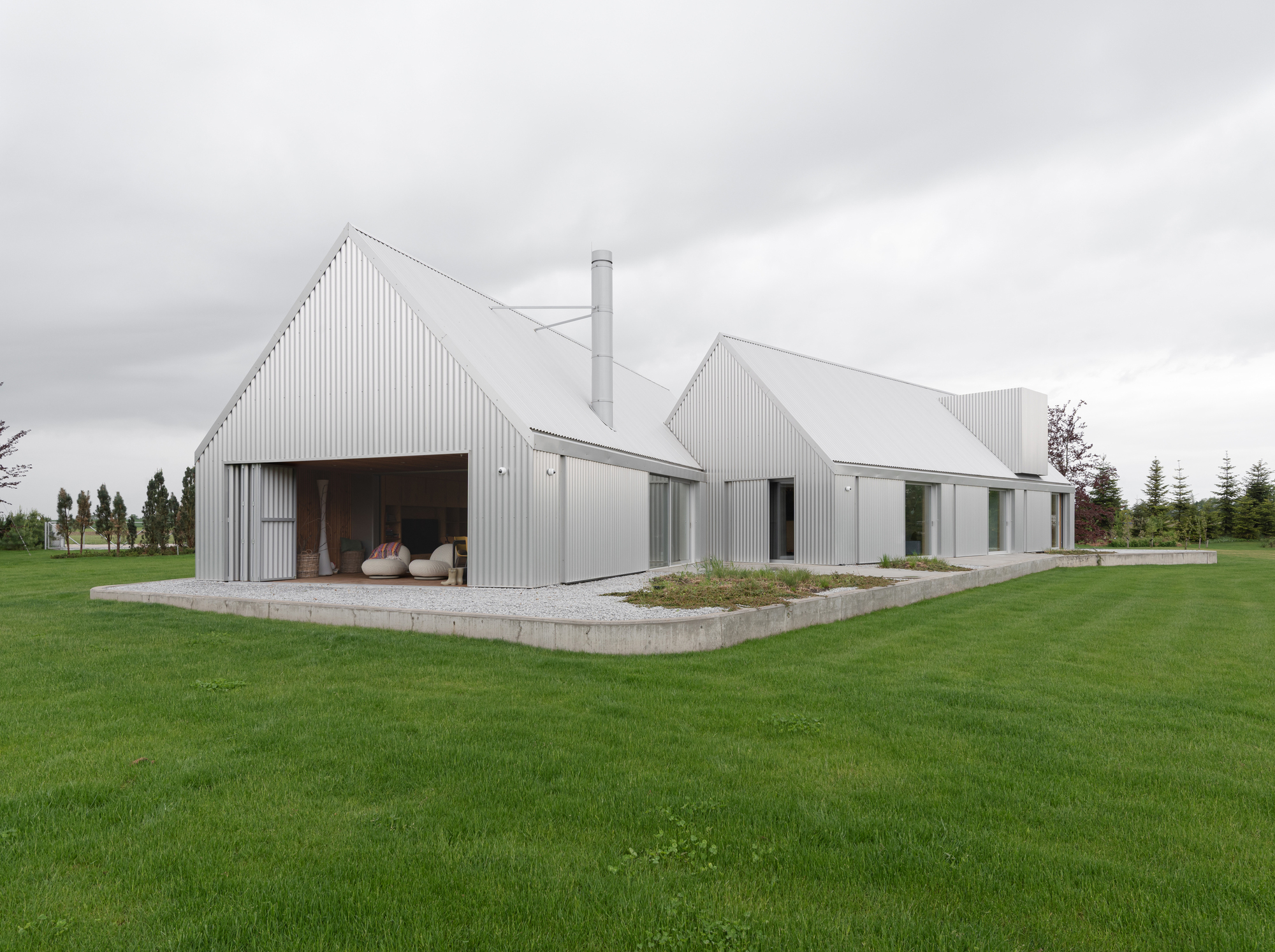 Cluster of corrugated metal gabled volumes on a concrete plinth surrounded by lawn under overcast skies