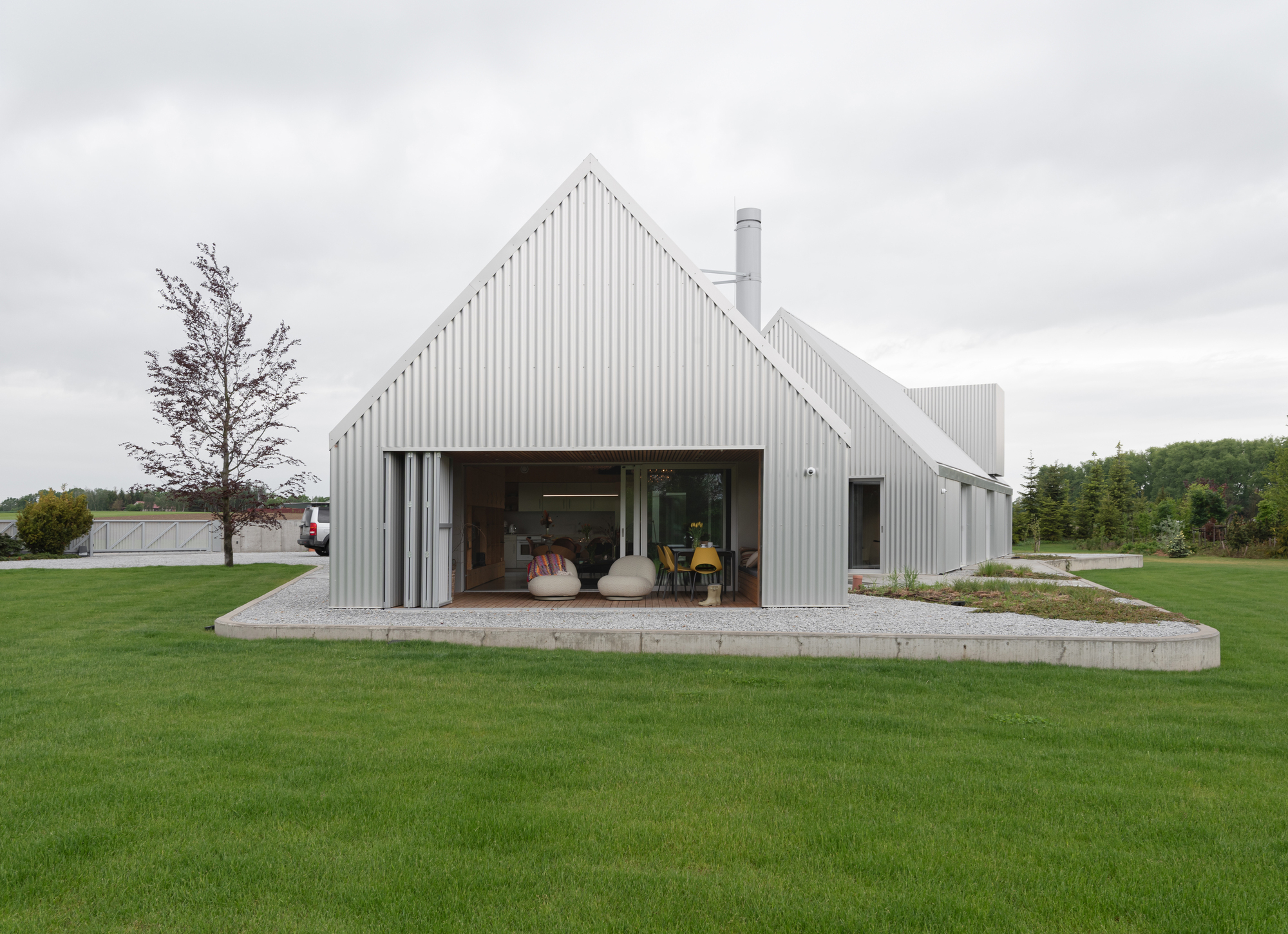 Front gable with large opening onto terrazzo terrace revealing interior living space and a single tree