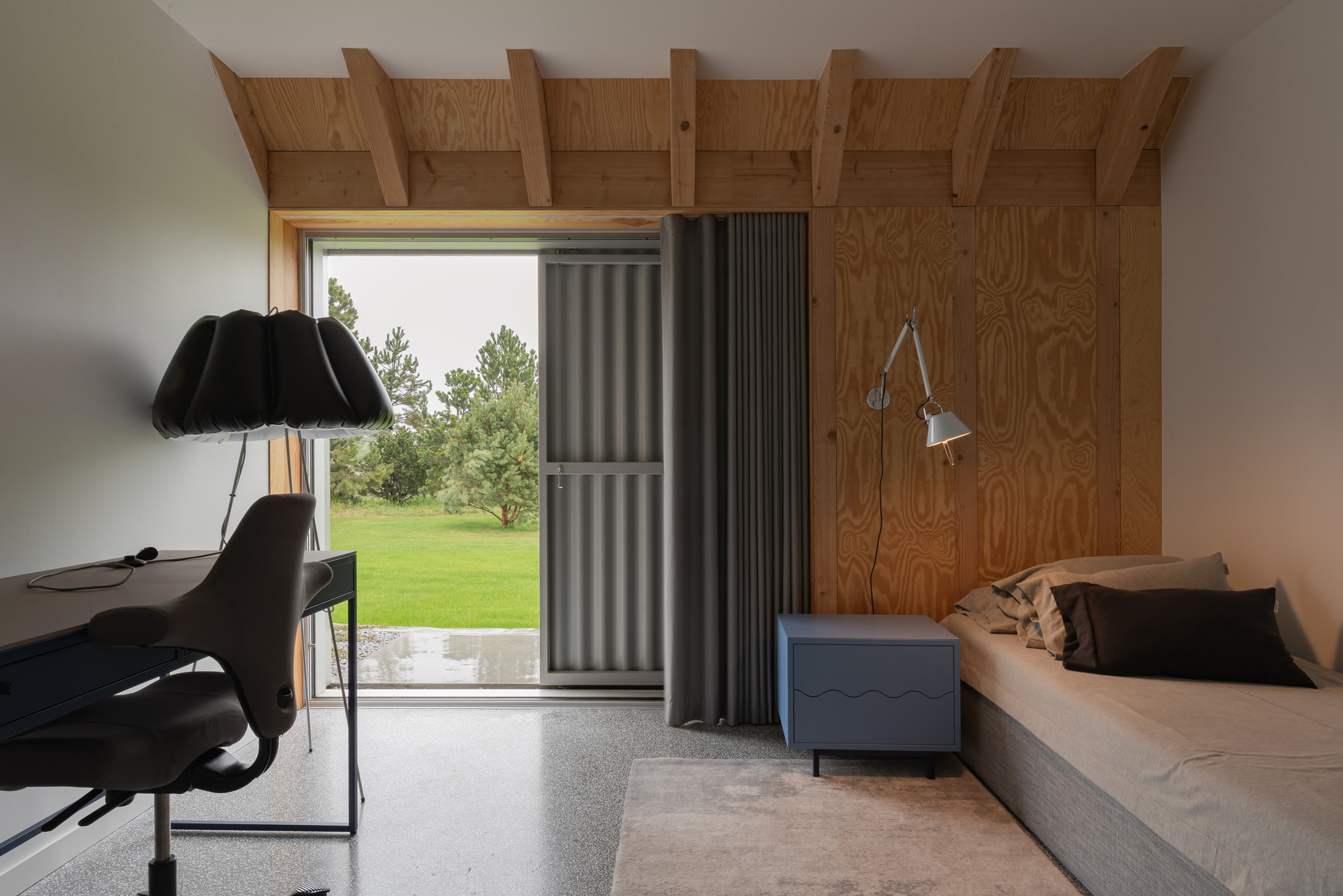 Bedroom with exposed timber rafters, plywood wall, and sliding metal door opening to lawn