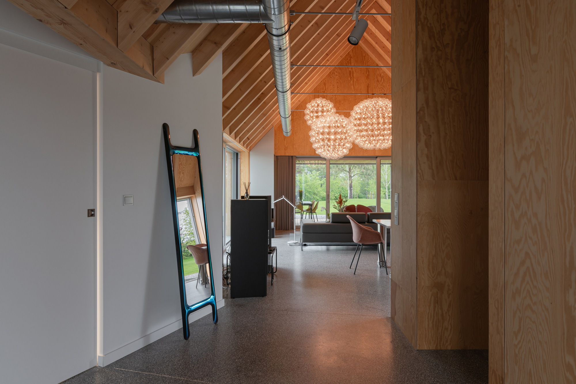 Interior hallway with exposed ductwork and diagonal timber ceiling panels leading toward glazed living area