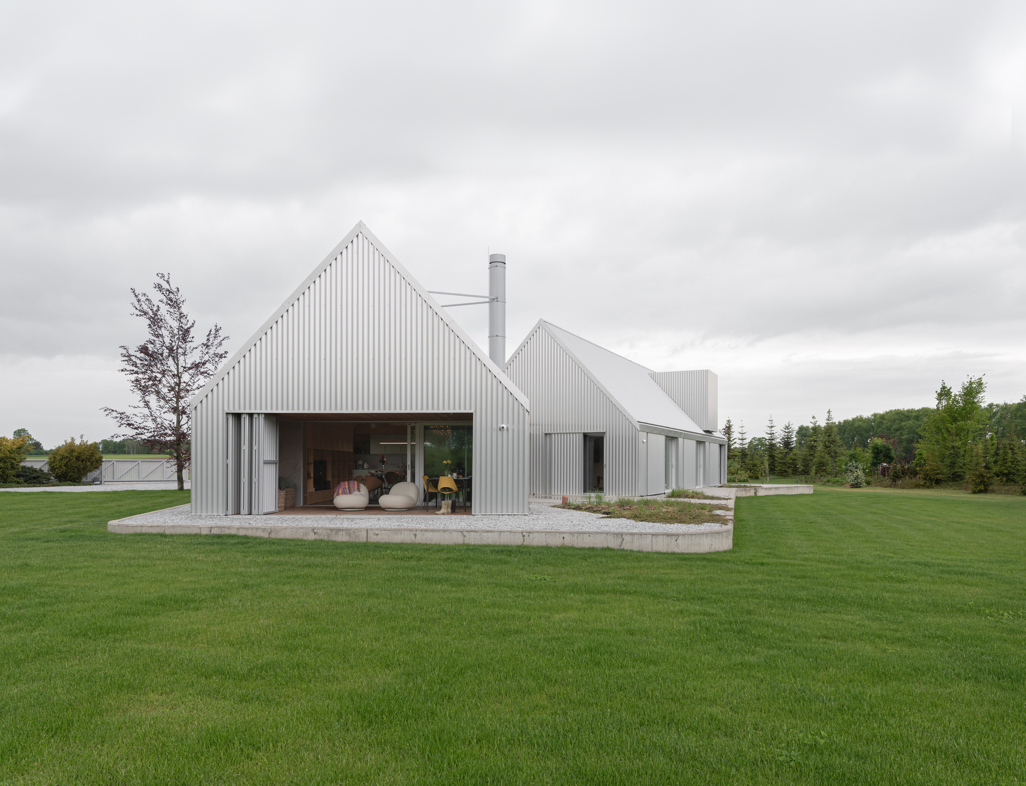 Metal-clad facade with open living pavilion on raised concrete terrace set in expansive green field