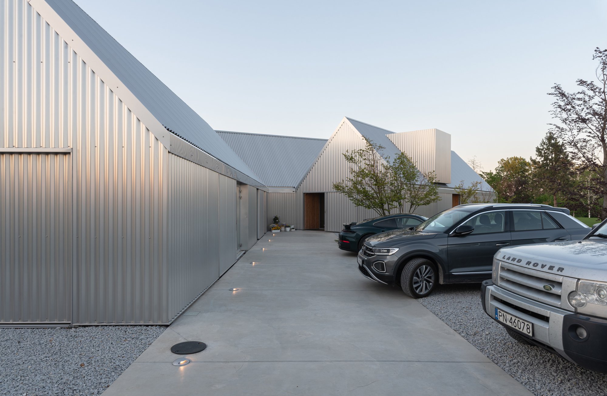 Corrugated metal driveway wall with recessed ground lights and parked cars at twilight