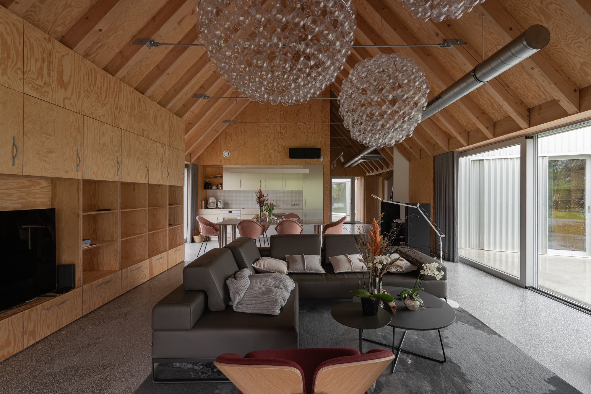 Open plan living space with exposed timber rafters, plywood wall and glass chandeliers