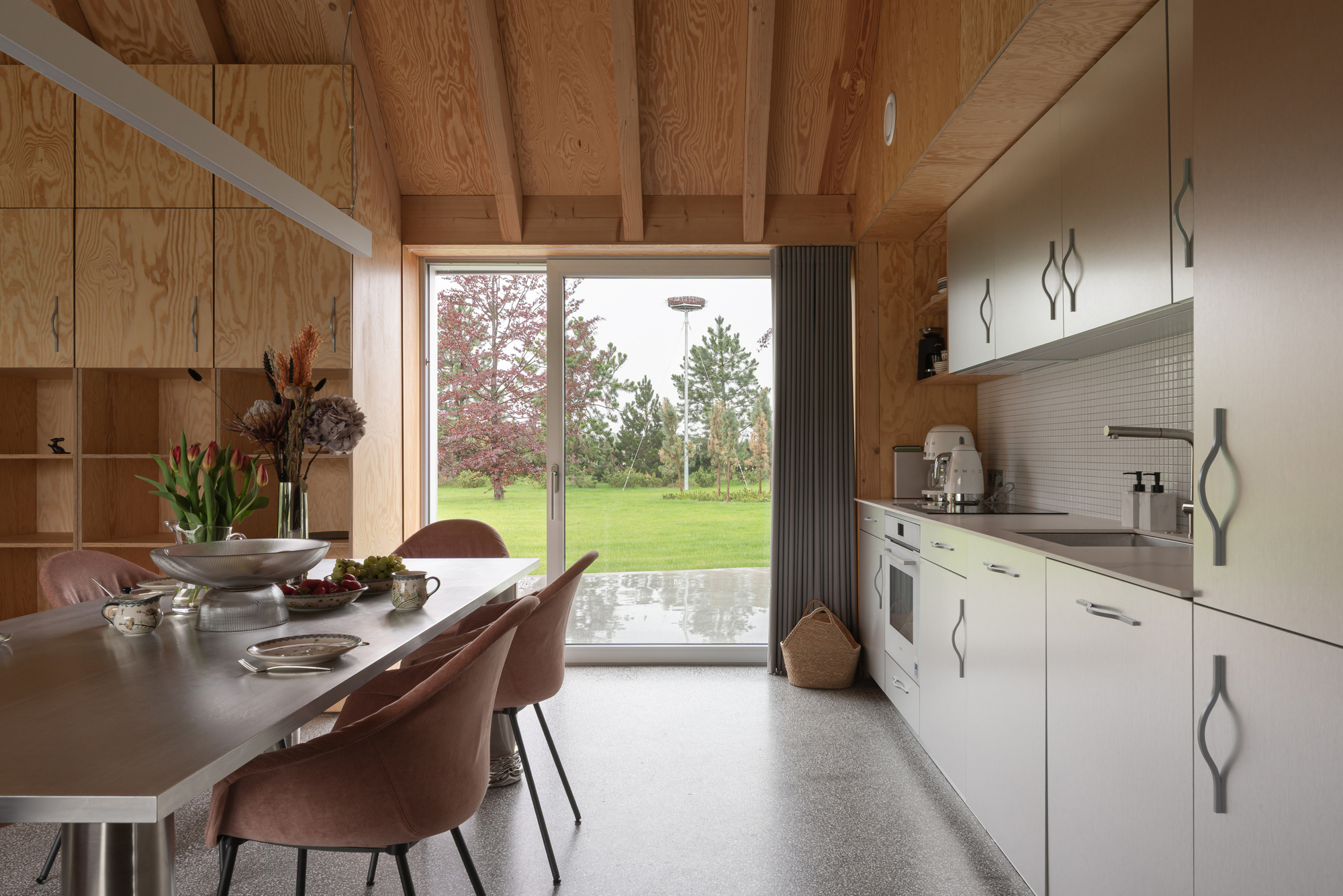 Kitchen with white tile backsplash and dining area framed by plywood walls and exposed beams
