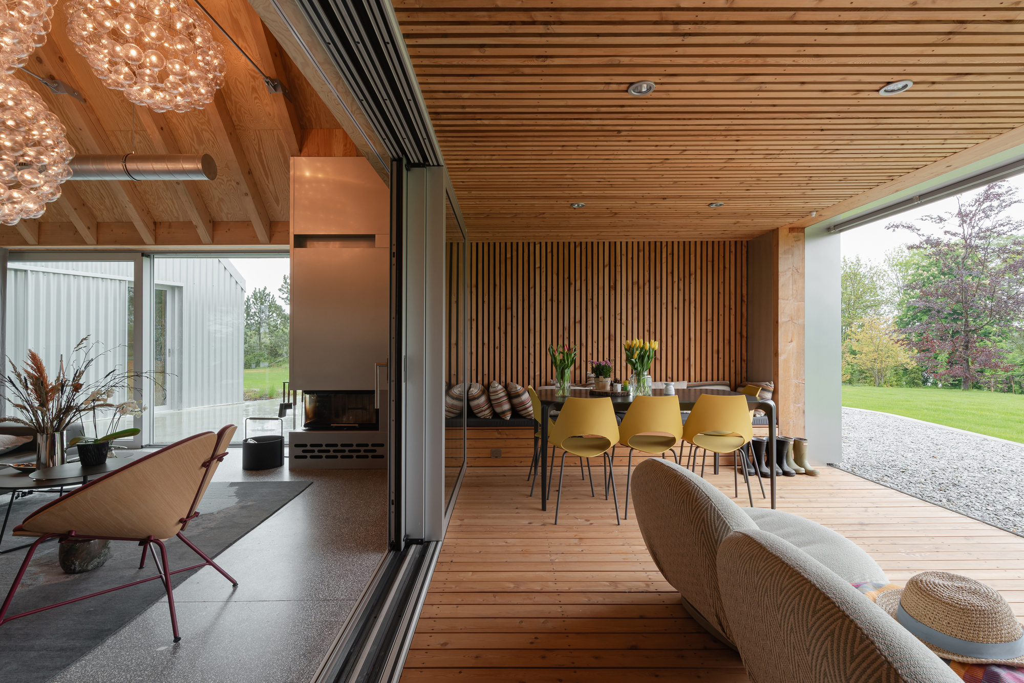 Covered terrace with slatted timber ceiling opening to a lawn through sliding glass doors
