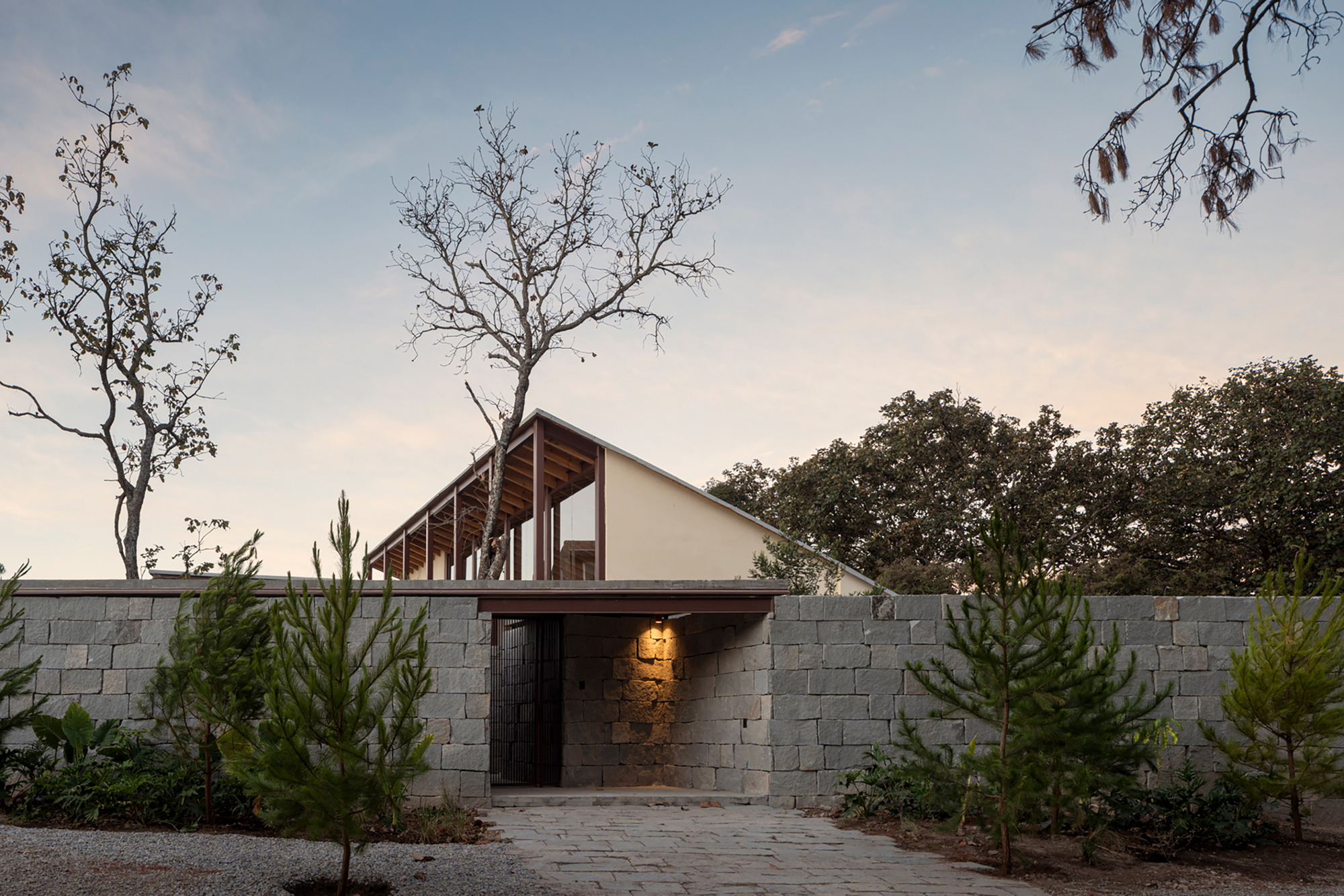 Street entrance through a grey concrete block wall with small pine trees at dusk