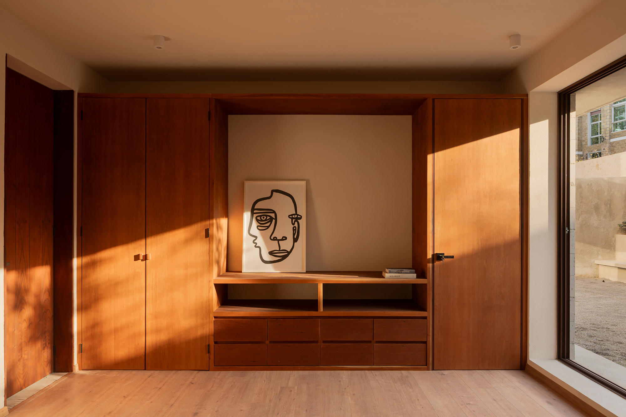 Built-in timber credenza and wardrobe wall with warm afternoon light from a courtyard window