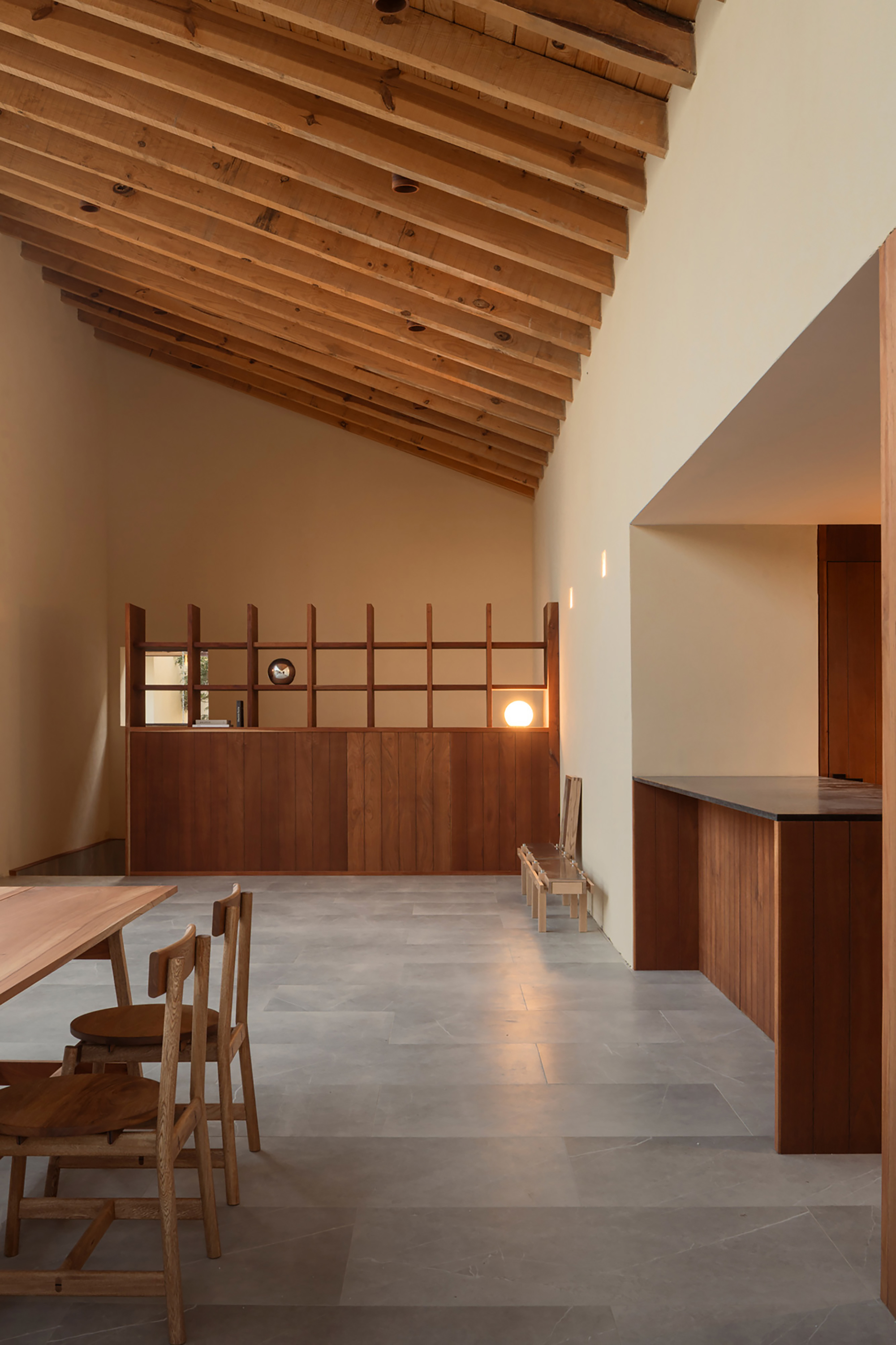Open living space with exposed timber ceiling beams and gridded timber storage wall