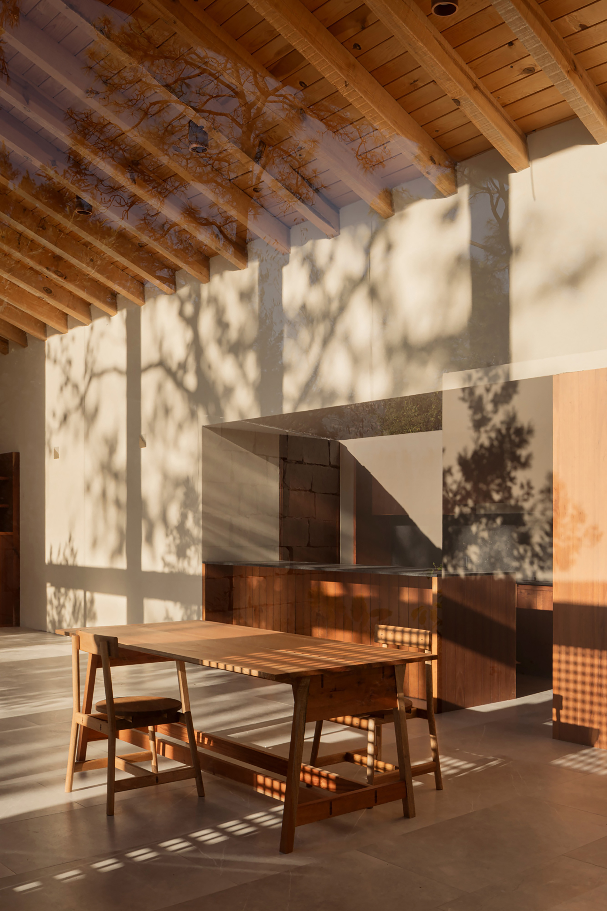 Dining area with exposed timber ceiling and dappled tree shadows cast across white walls and tiled floor