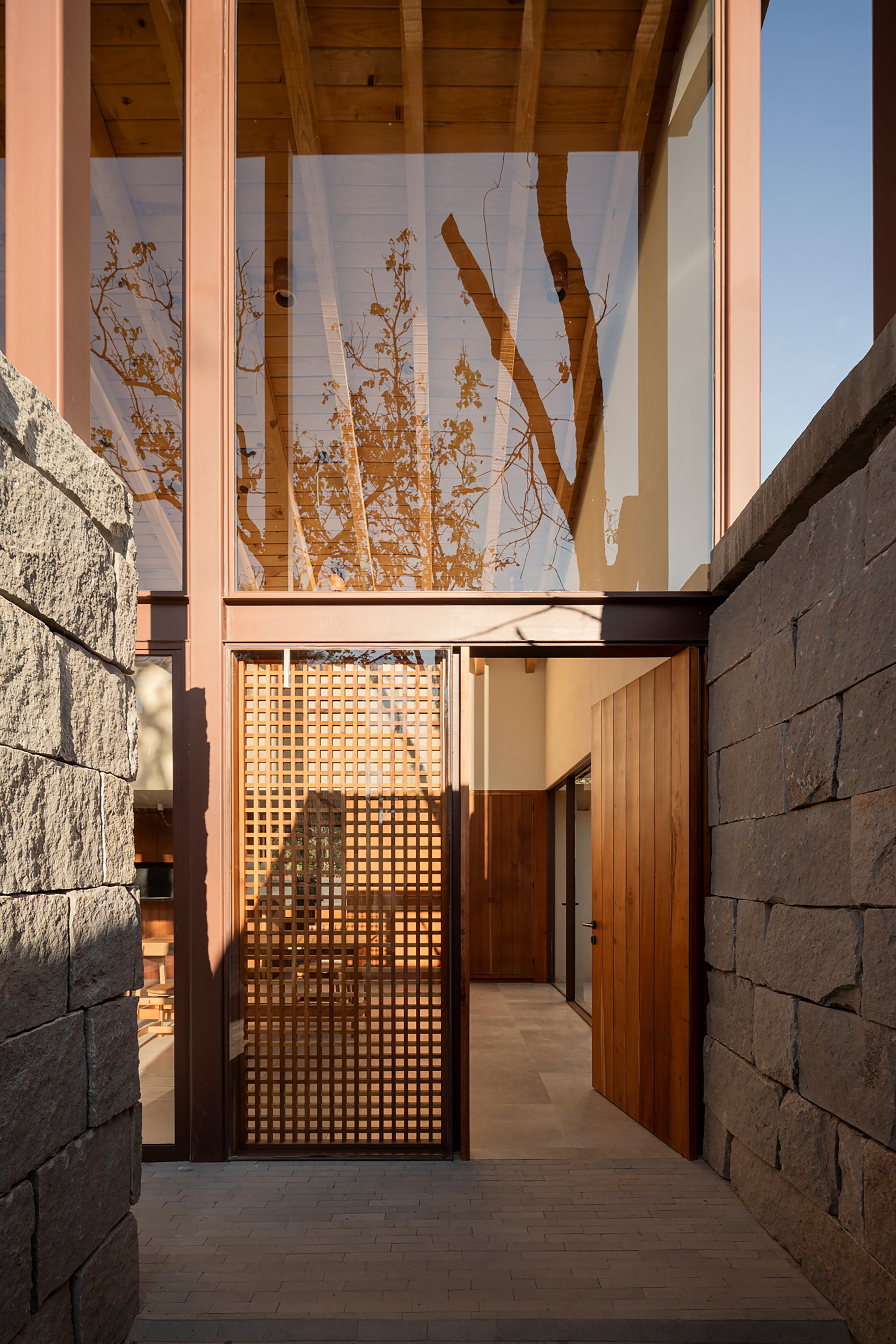 Entry passage with latticed timber gate between textured concrete walls under a timber-clad soffit at sunset