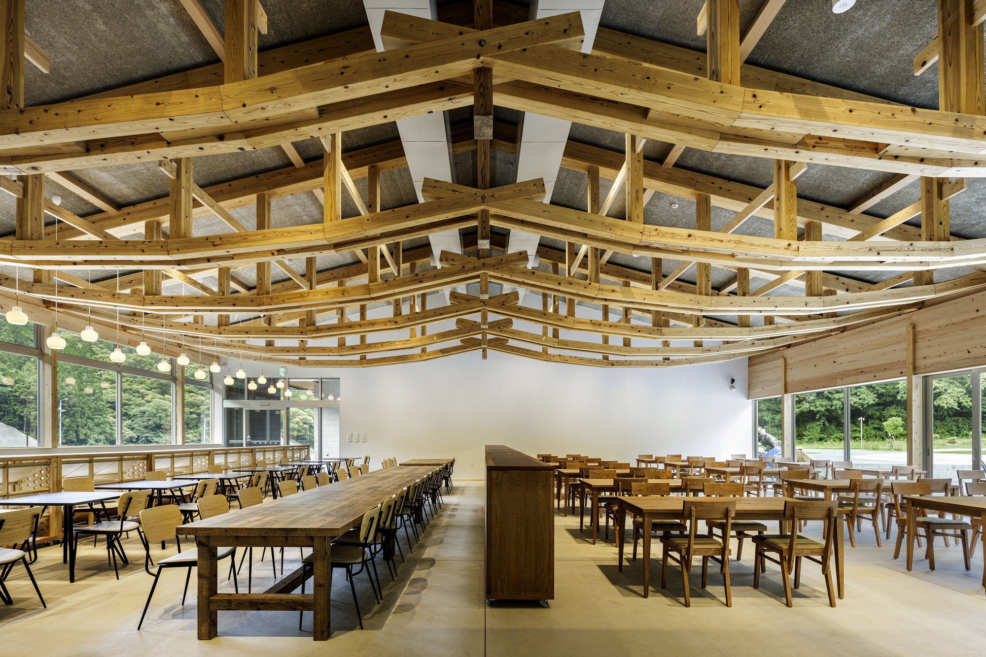 Dining hall with exposed timber truss system curving above communal tables and pendant lights