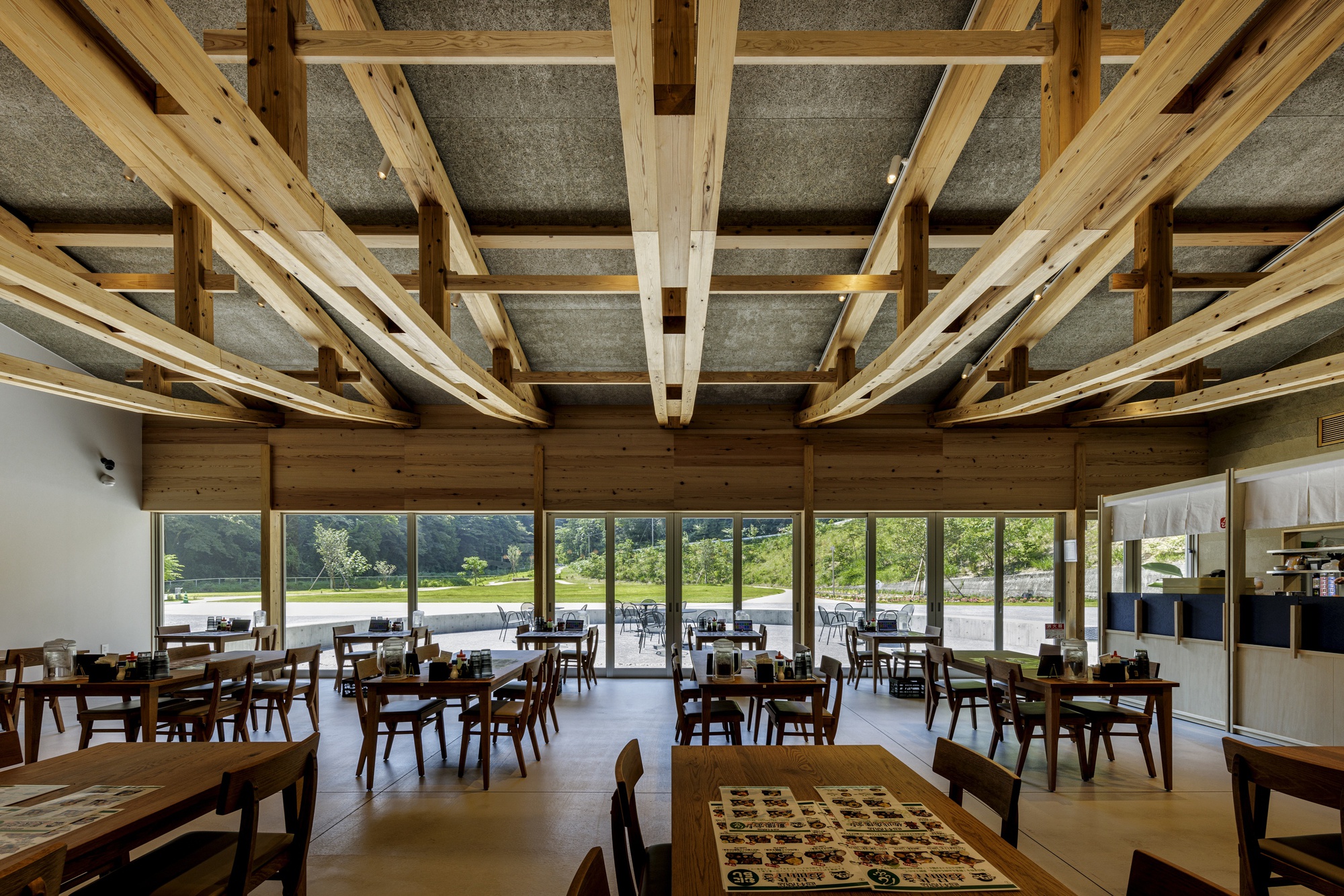 Interior view of the curved timber roof framing and full-height glazing overlooking the parking area