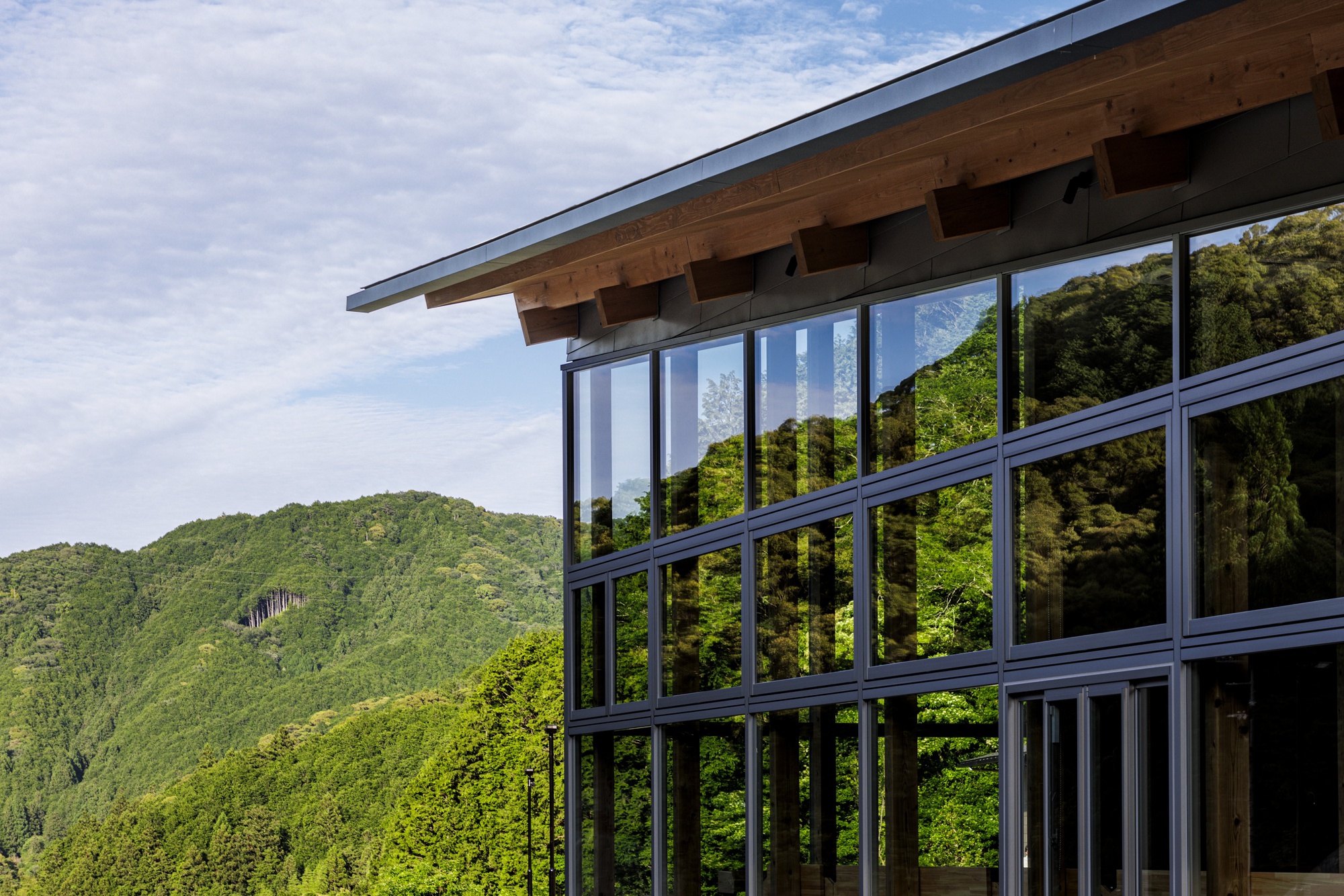 Corner detail of the timber eave and full-height glazed facade reflecting the surrounding forested hillside