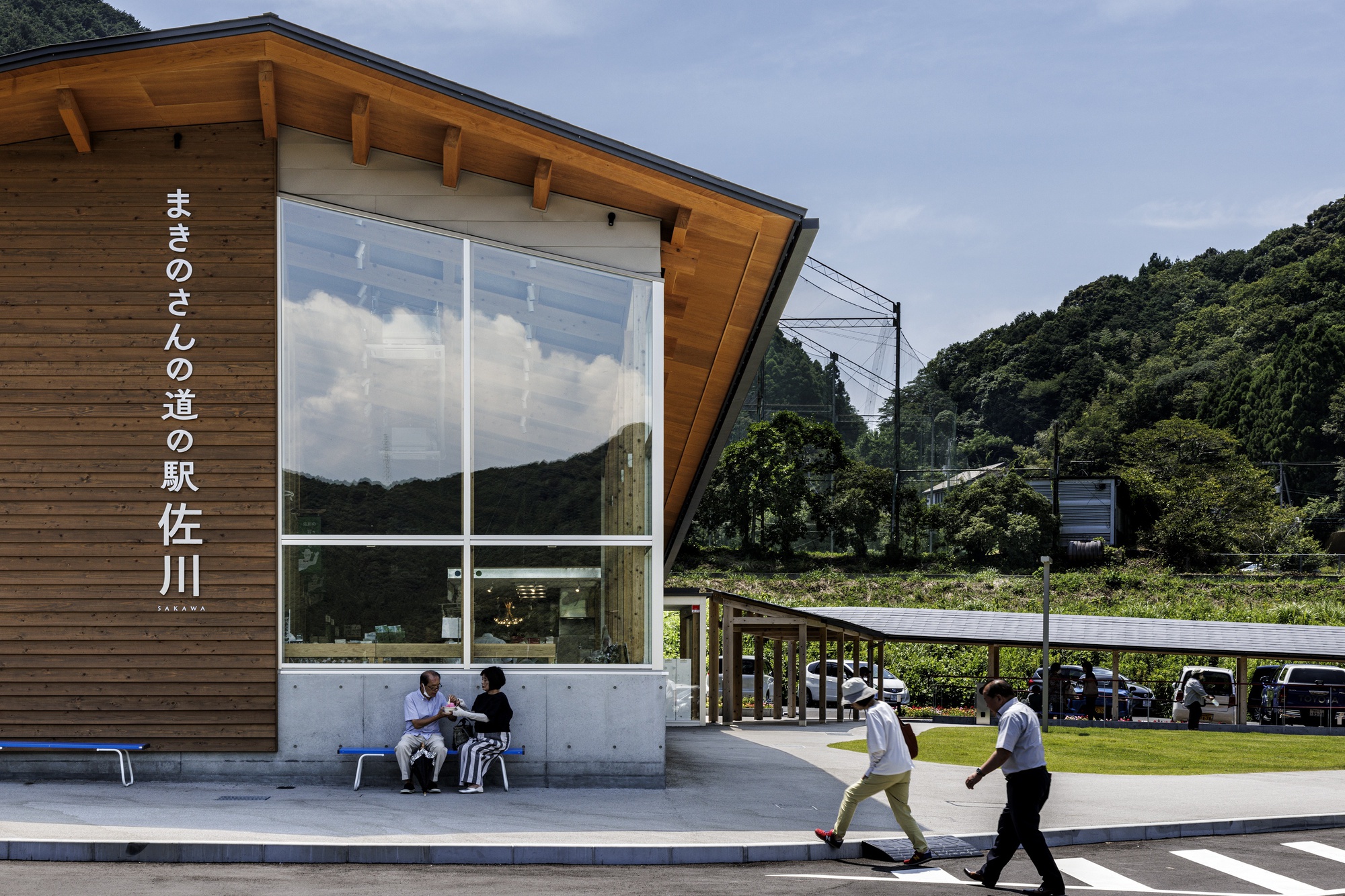 Angled timber-clad entrance pavilion with large glazed corner and people sitting beneath overhang