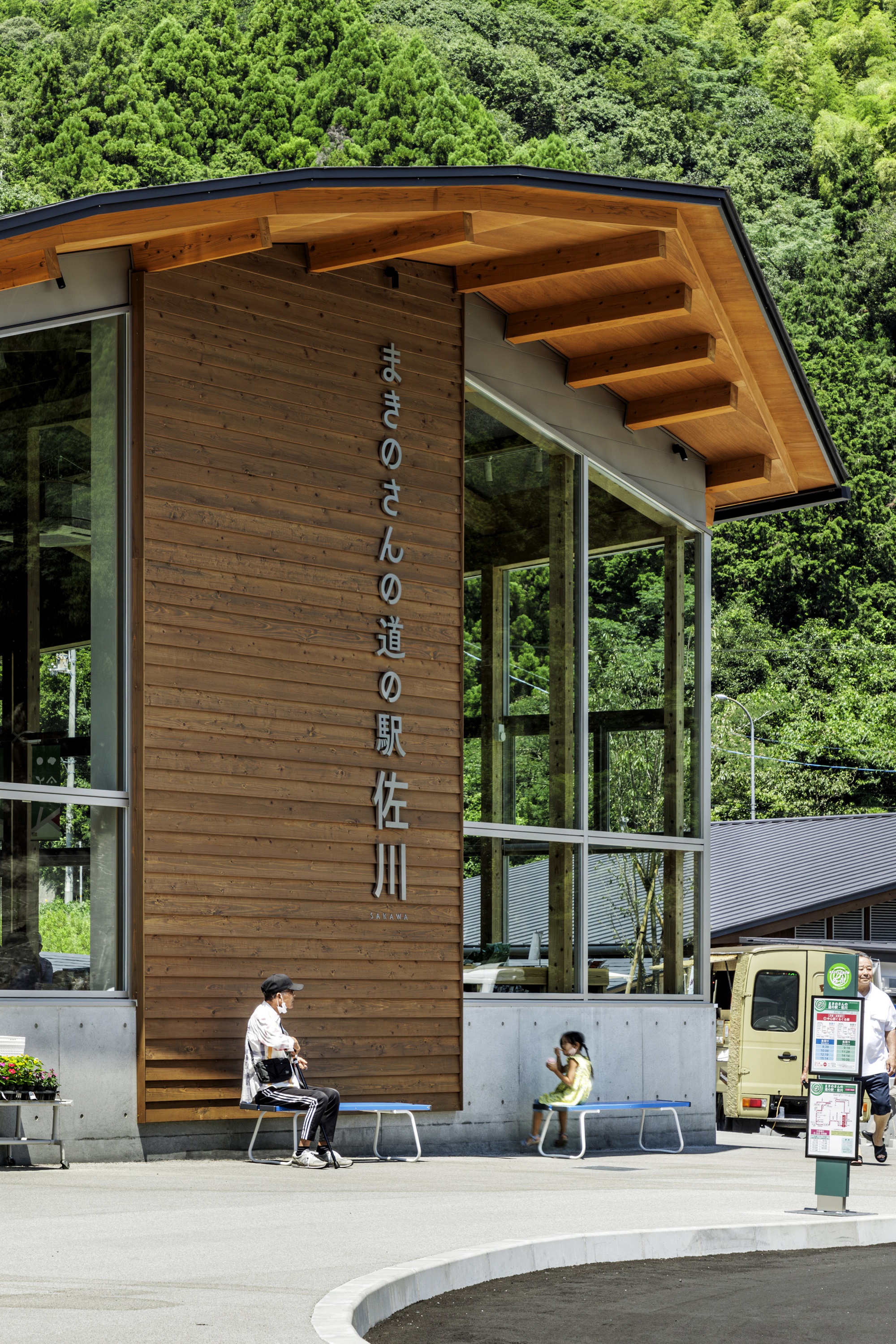 Timber entrance volume with projecting roof beams and glazed walls while visitors occupy benches below