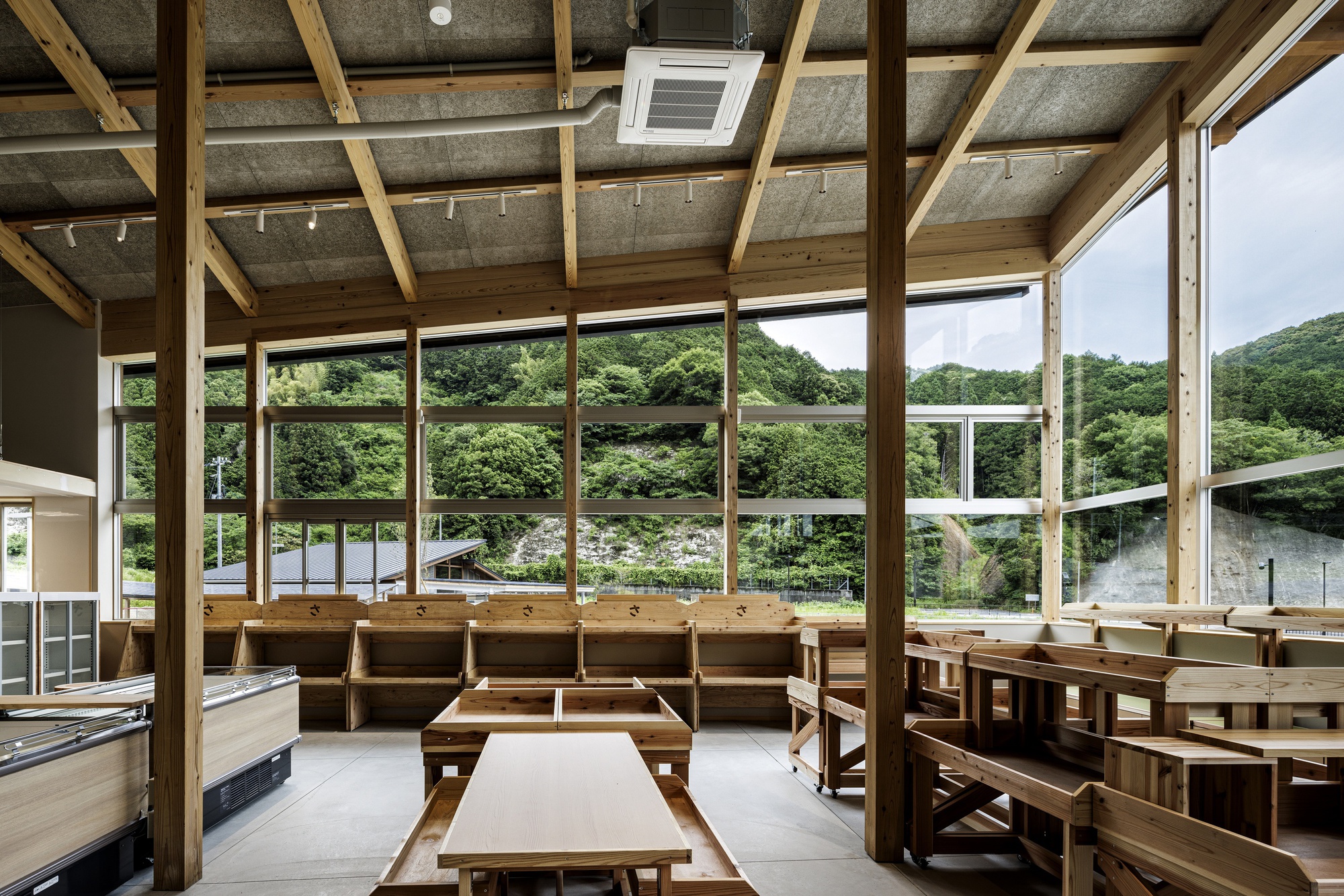 Interior dining space with exposed timber roof structure, full-height glazing overlooking river and green valley