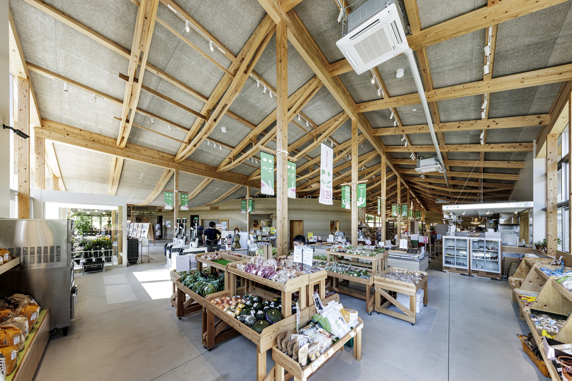 Market hall with wooden produce tables and shoppers beneath curved timber rafters and hempcrete ceiling