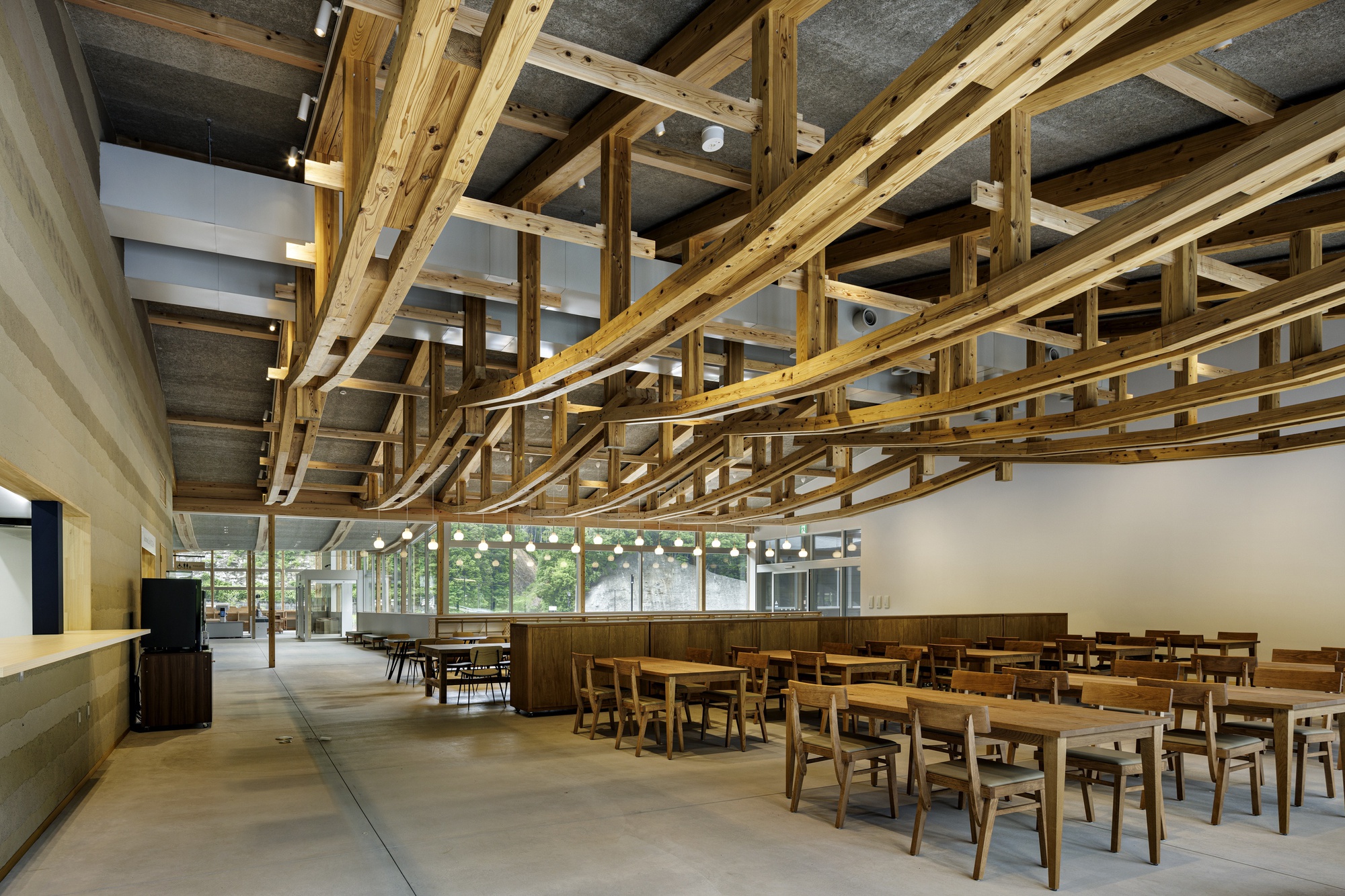 Open dining area with intersecting timber trusses overhead, concrete ceiling inserts, and rows of wooden tables and chairs