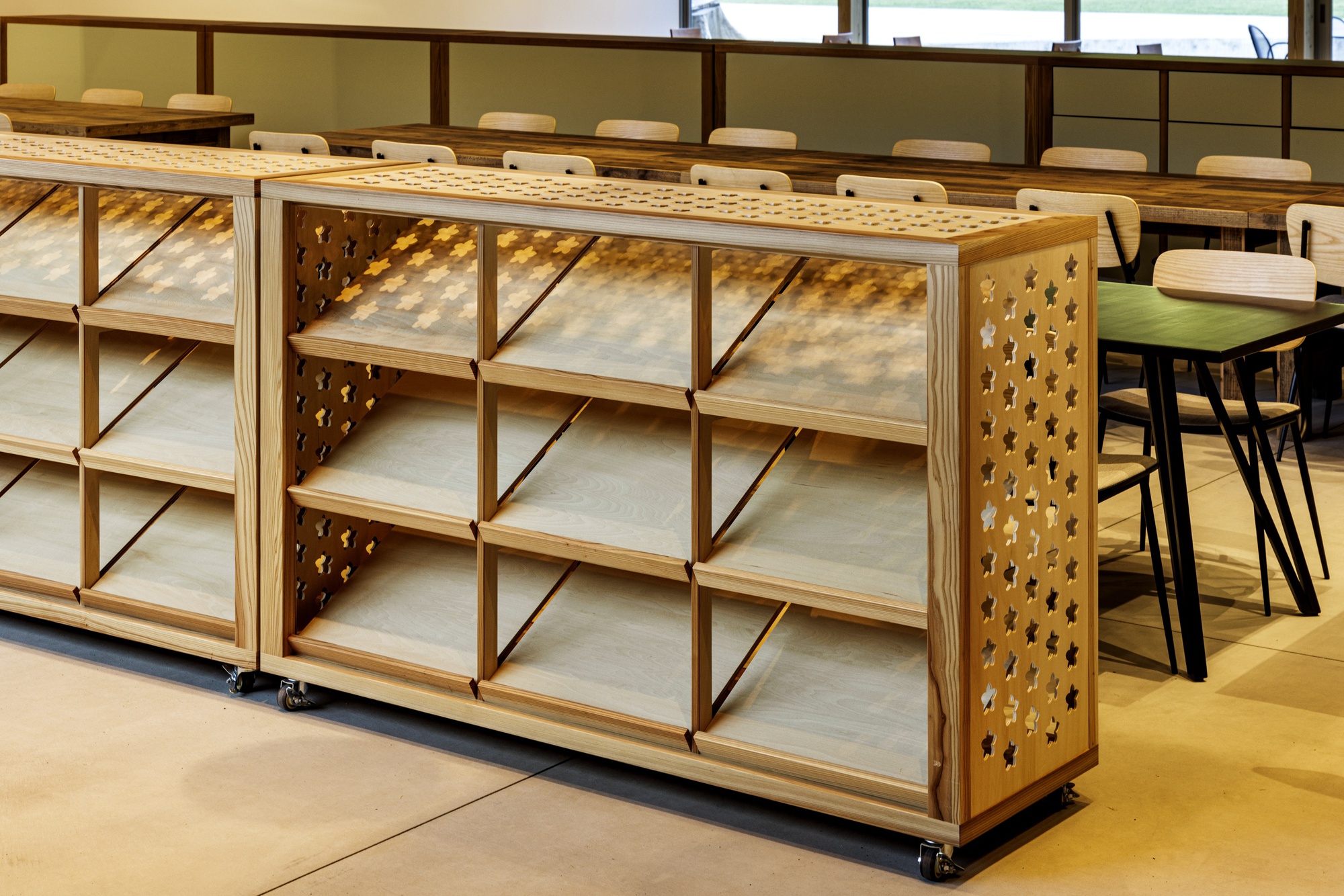 Mobile plywood shelving units with perforated side panels and angled dividers in a dining area