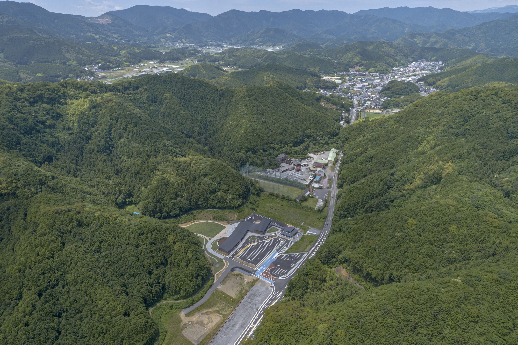 Aerial view of the facility compound nestled in a forested valley with winding roads
