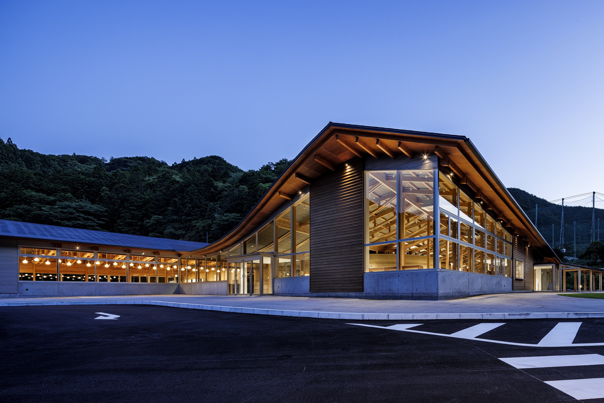 Corner view of the glass-walled timber structure with exposed rafters under a blue evening sky