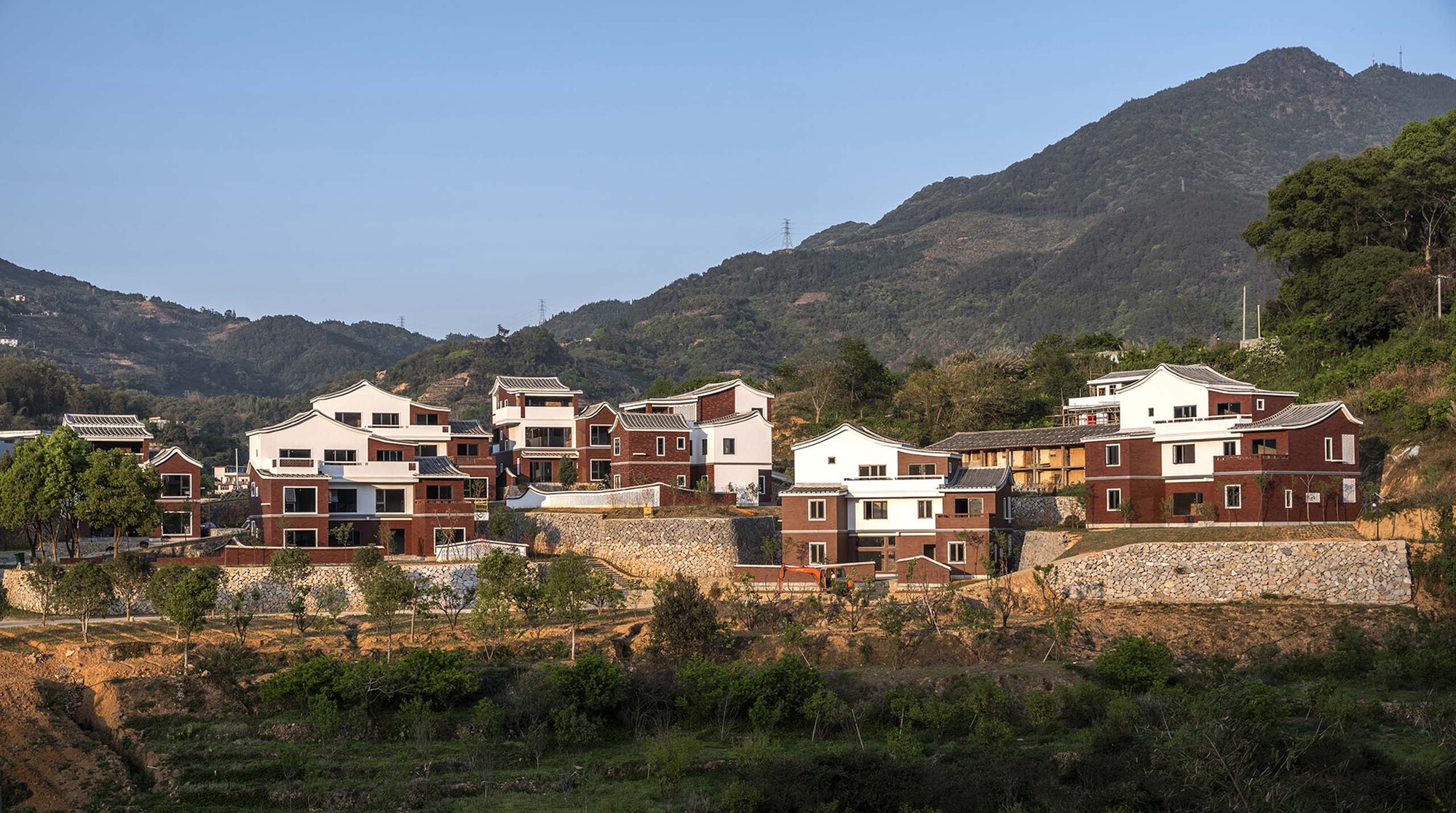 Cluster of red brick and white stucco houses on a hillside beneath a forested mountain
