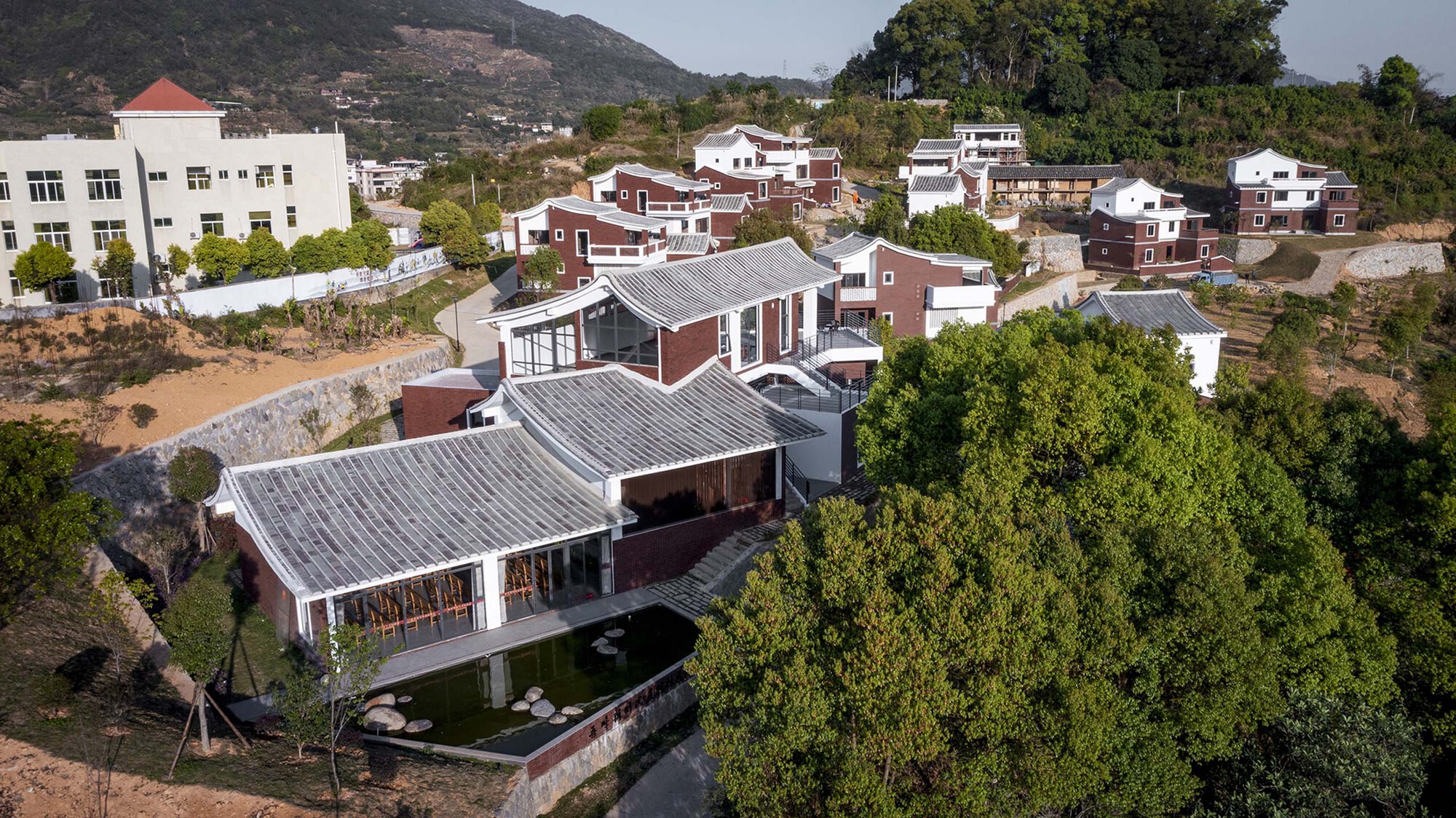 Aerial view of buildings with grey tile roofs surrounding a central courtyard pond and lawn