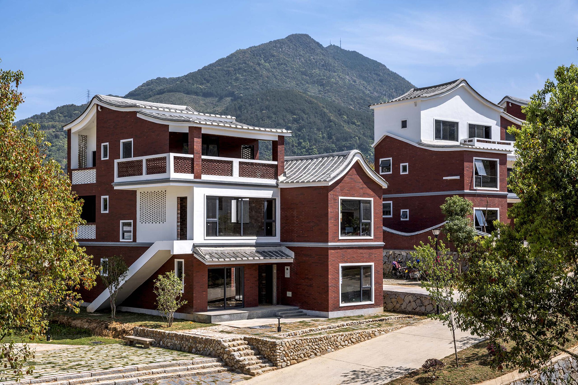 Front facade of clustered red brick and white volumes with curved tile roofs and terraced stone walls