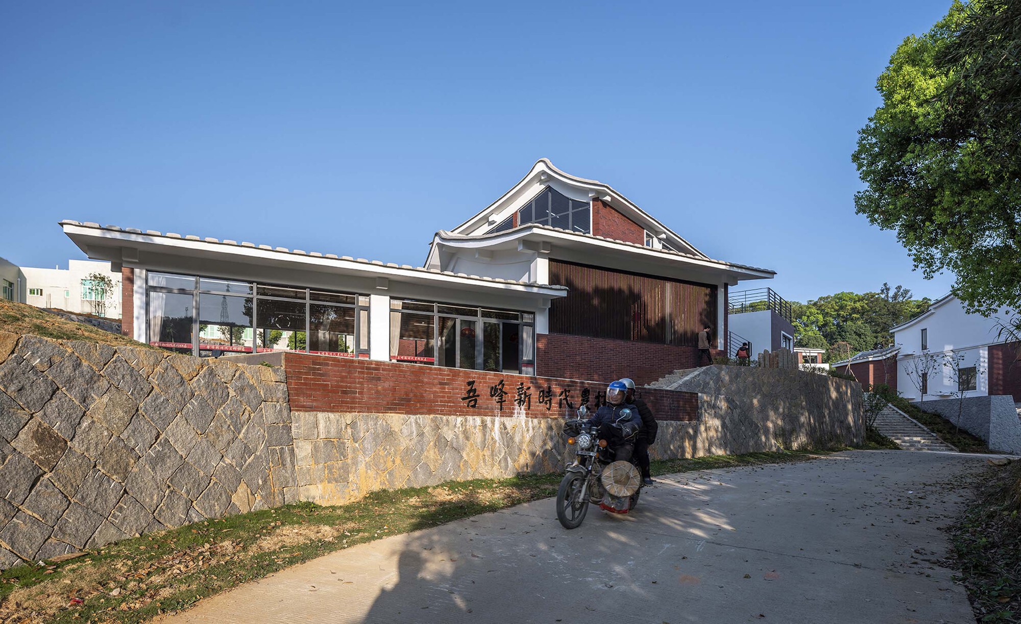 Street view of a low-slung building with glazed walls and curved tile roof as a motorcyclist passes