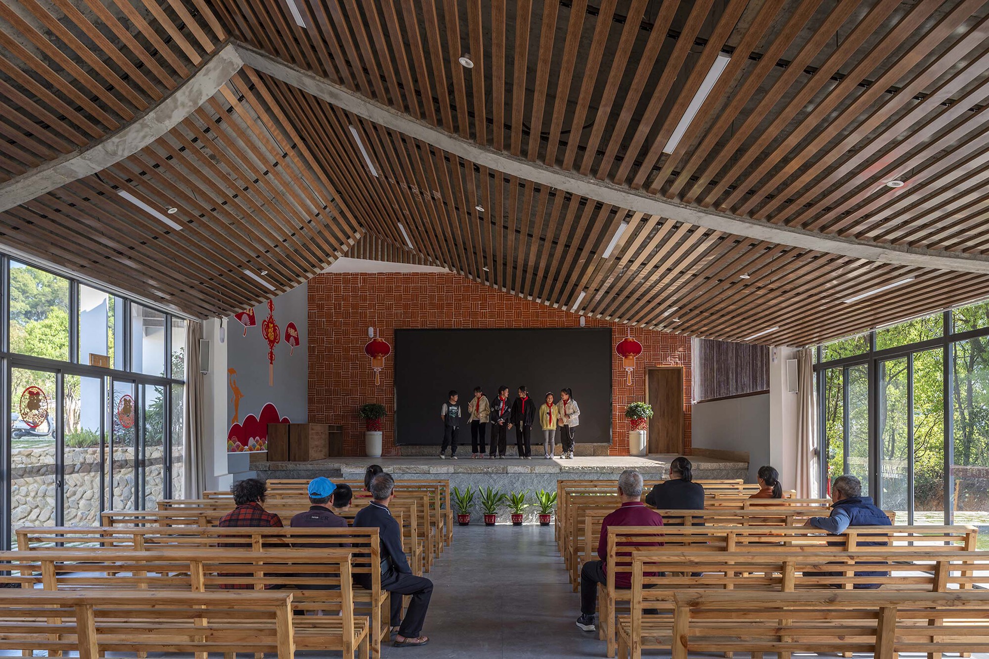 Interior hall with timber slat ceiling, wooden benches and a raised stage platform with brick chimney