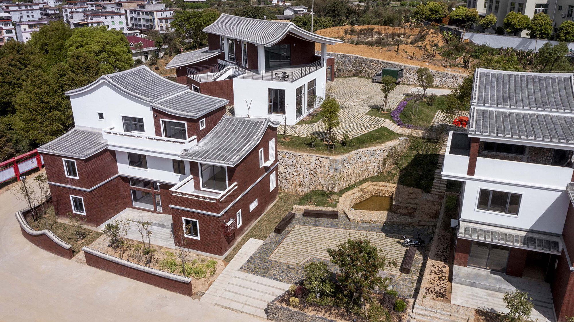Aerial view of clustered housing volumes with red brick cladding and curved metal roofs among terraced courtyards
