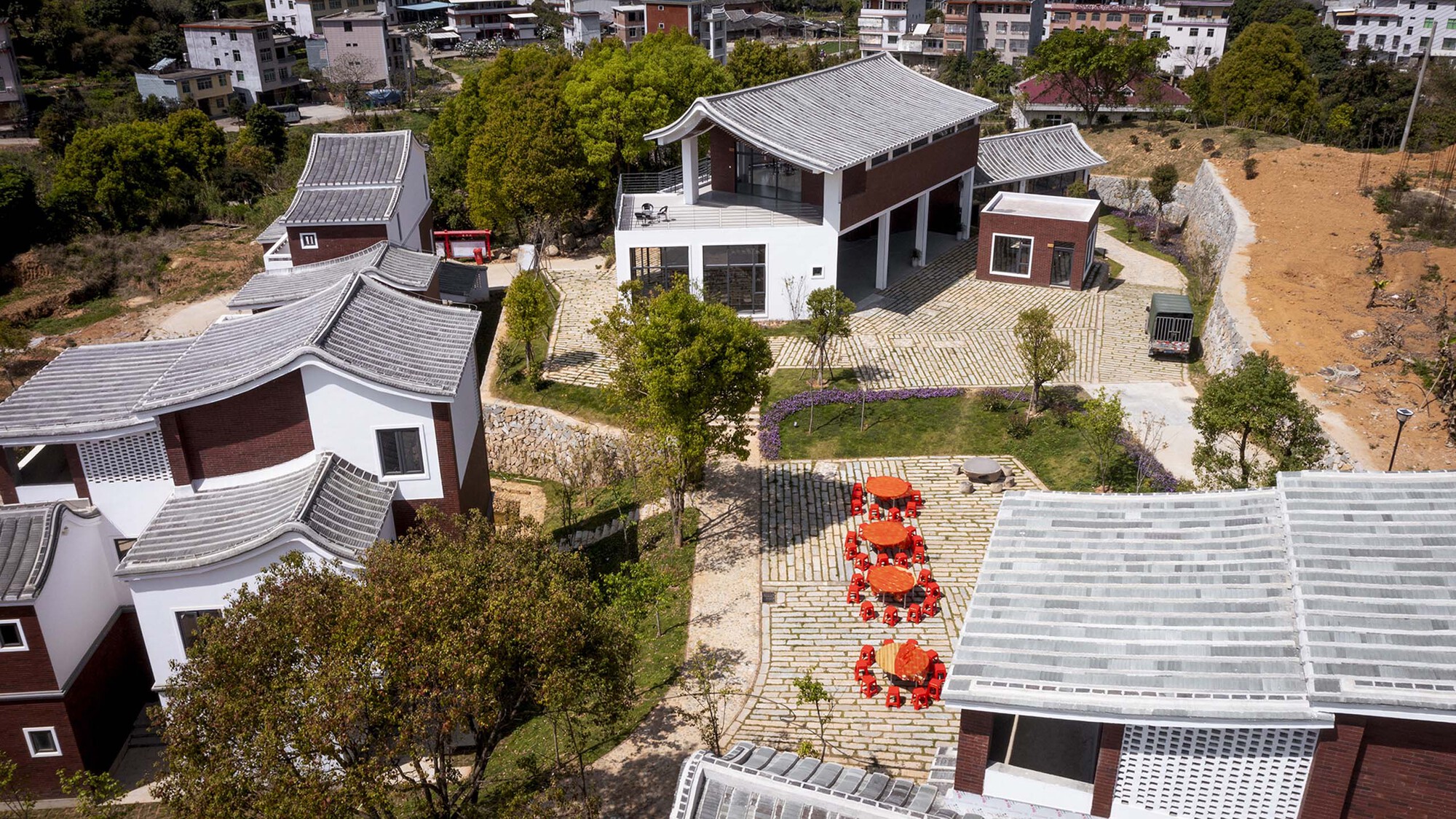 Overhead view of courtyard garden with red circular planters arranged along a stone paved path between houses