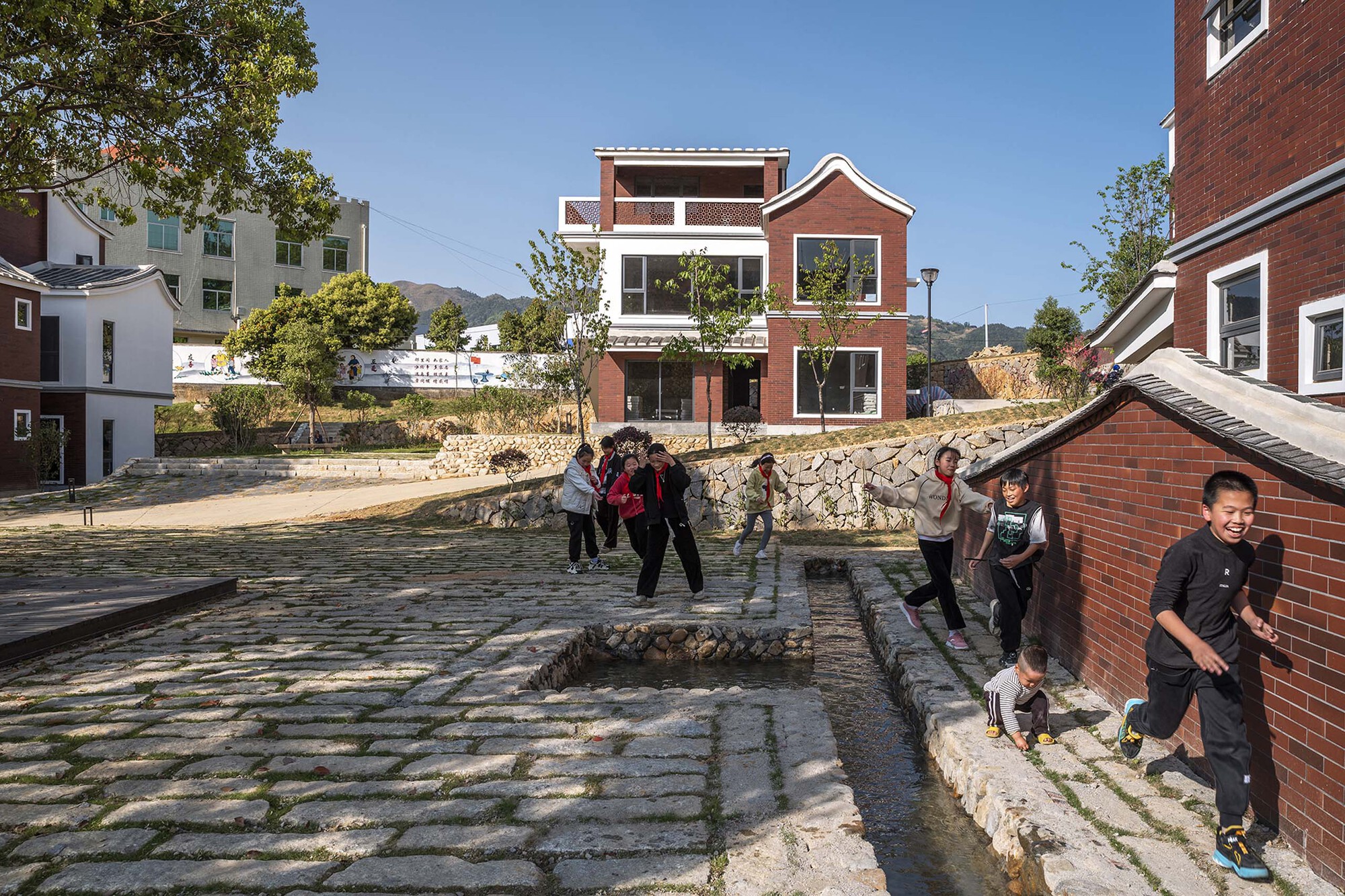 Stone paved courtyard with shallow water channel and children playing among brick houses