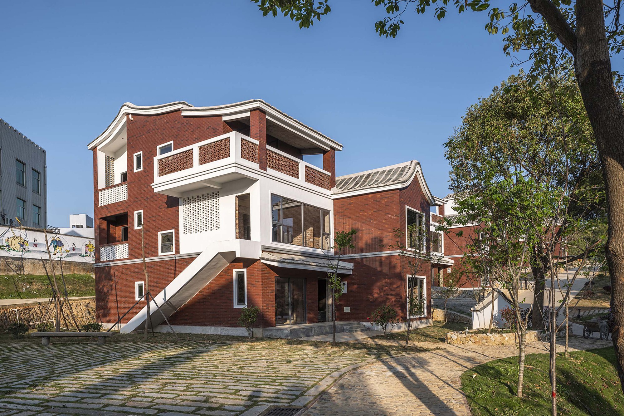 Three-story brick house with white balconies and perforated screens facing a stone courtyard