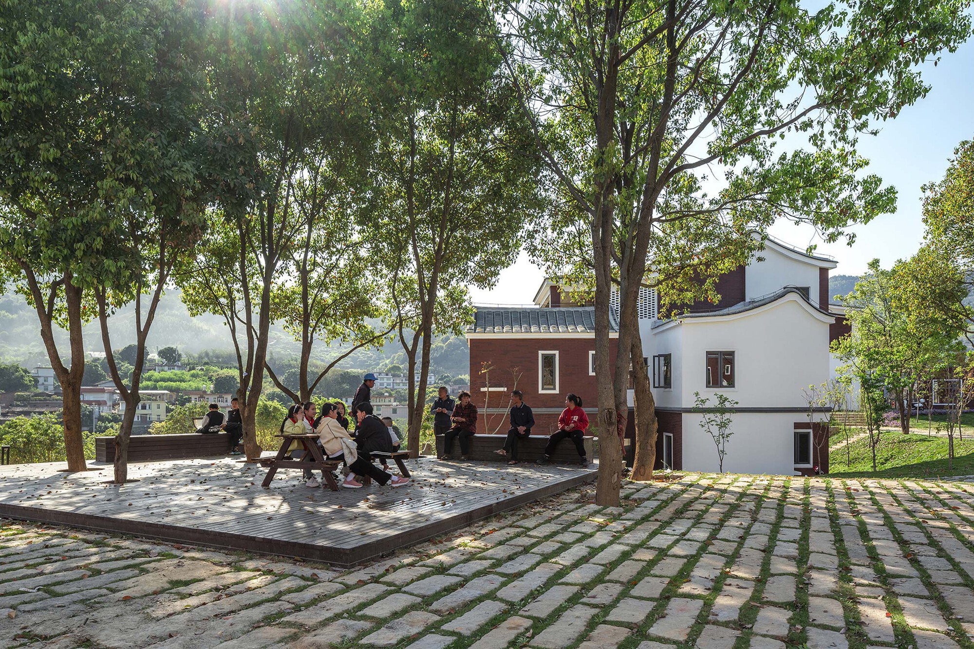 People seated on a shaded platform beneath mature trees overlooking the valley
